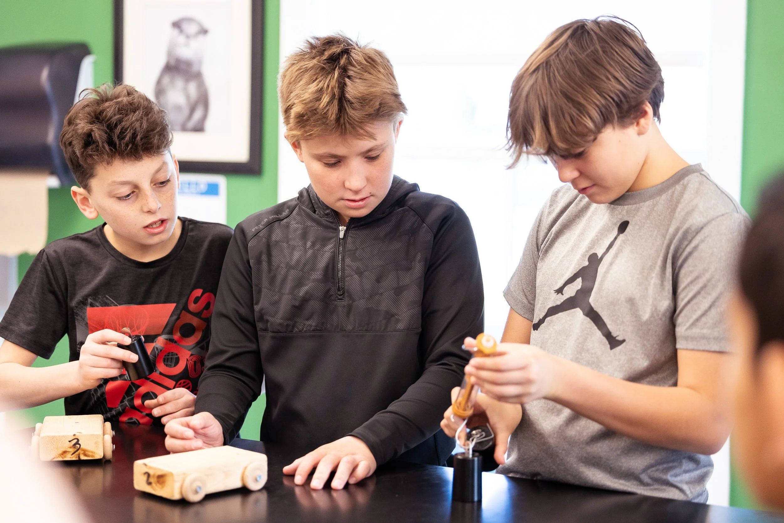 Three students gathered around a table working on a science project with small wooden vehicles at a private middle school in Boston.