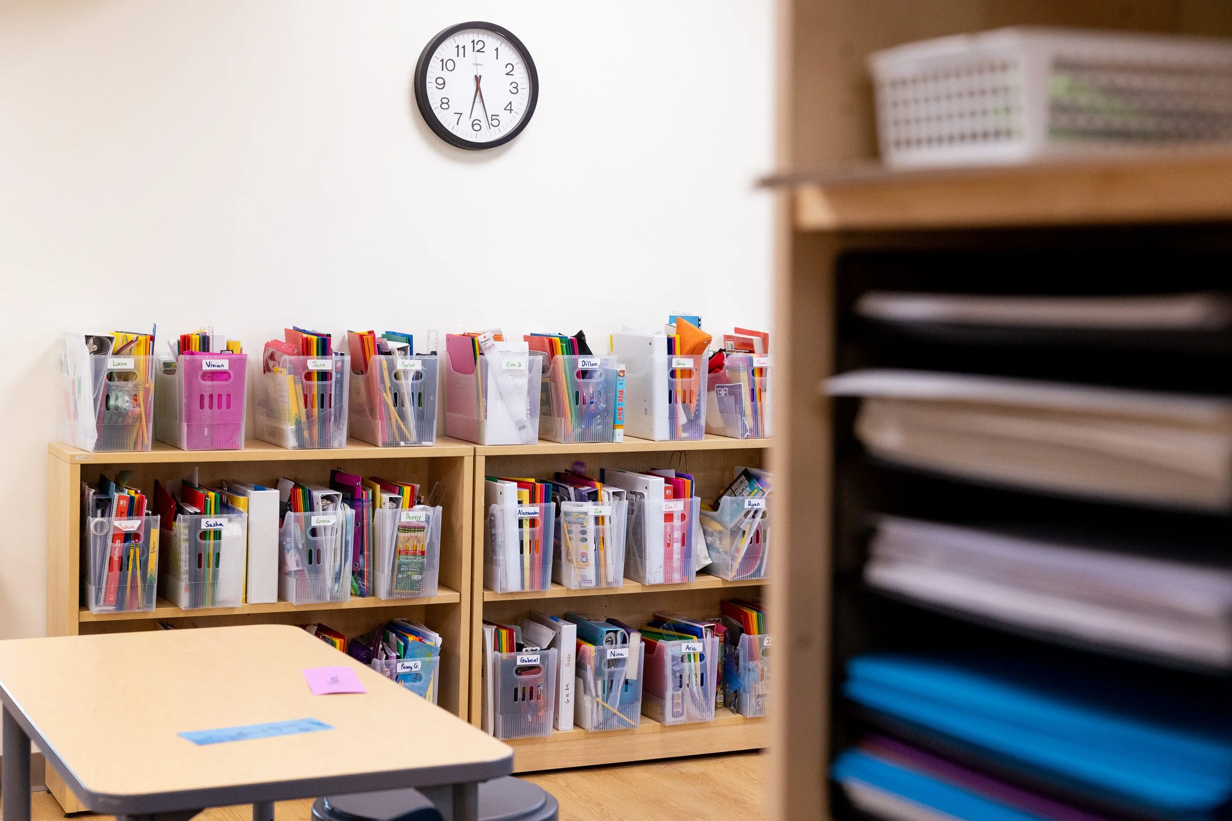 Montessori classroom with storage shelves filled with colorful binders and folders and a small table with papers.