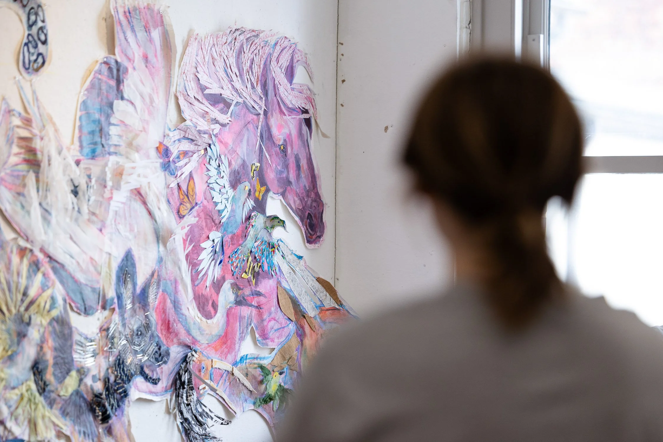 Person viewing a colorful mixed-media collage of various animals on a wall in art studio.