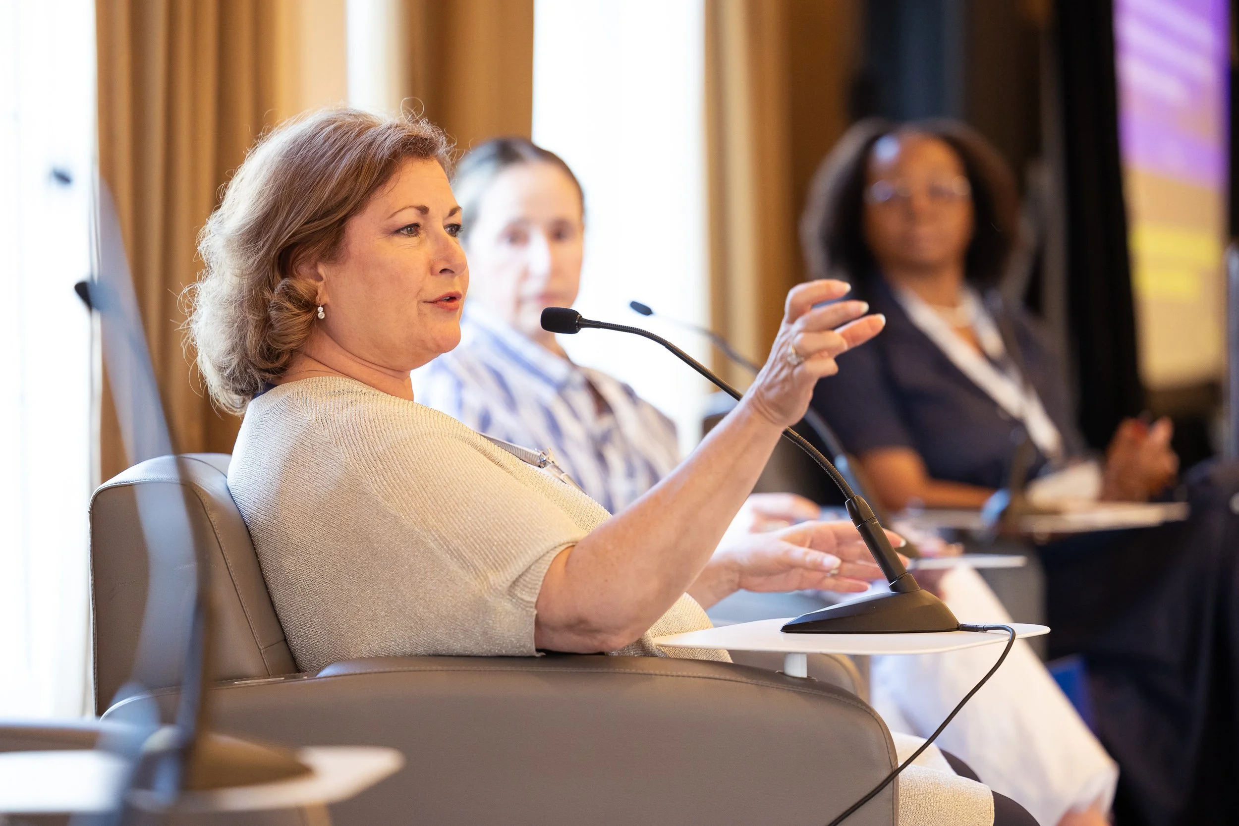 A woman speaking into a microphone at a panel discussion at Boston biotech law conference.