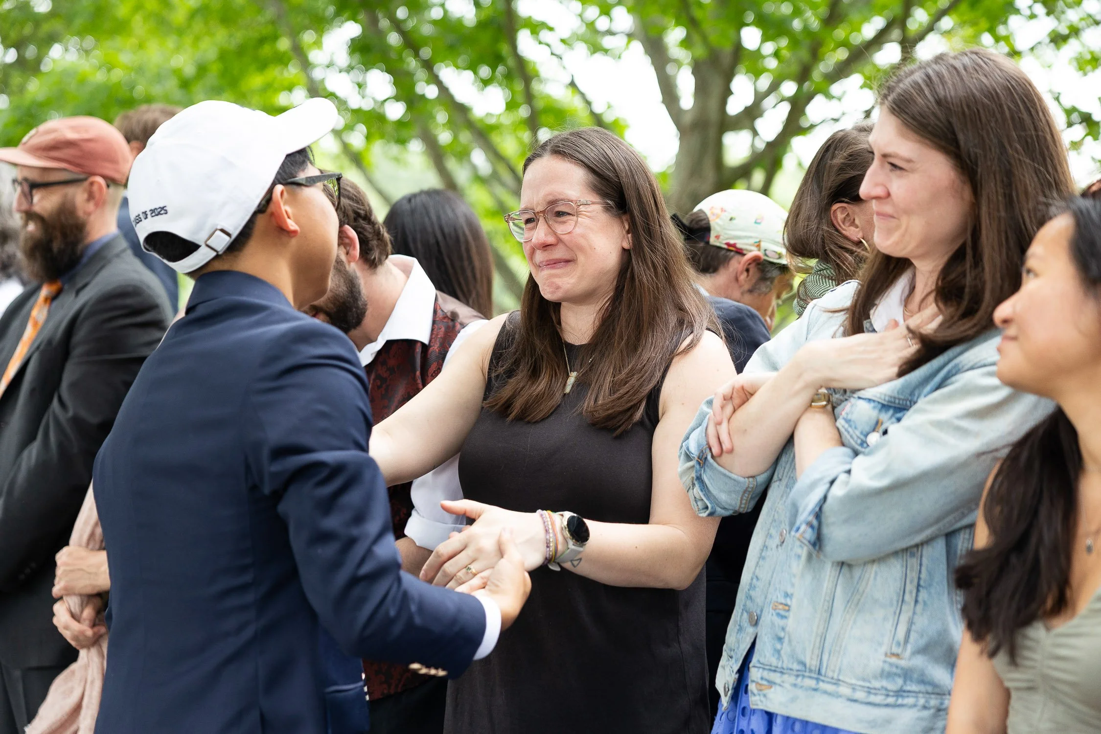 A teacher is emotional while shaking hands with a high school graduate.