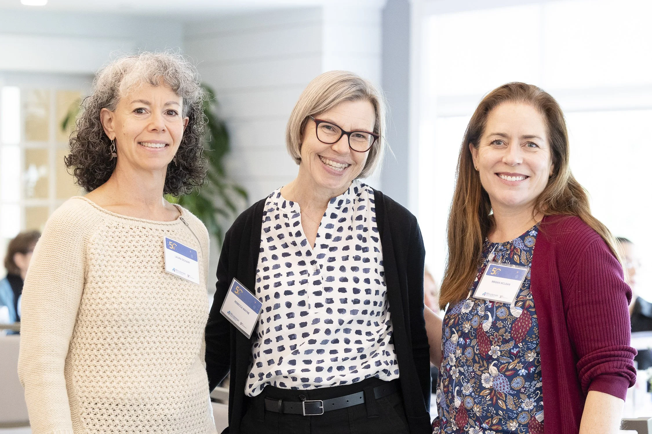 Three women smiling at a nonprofit event, wearing name badges, in Lincoln, Massachusetts.