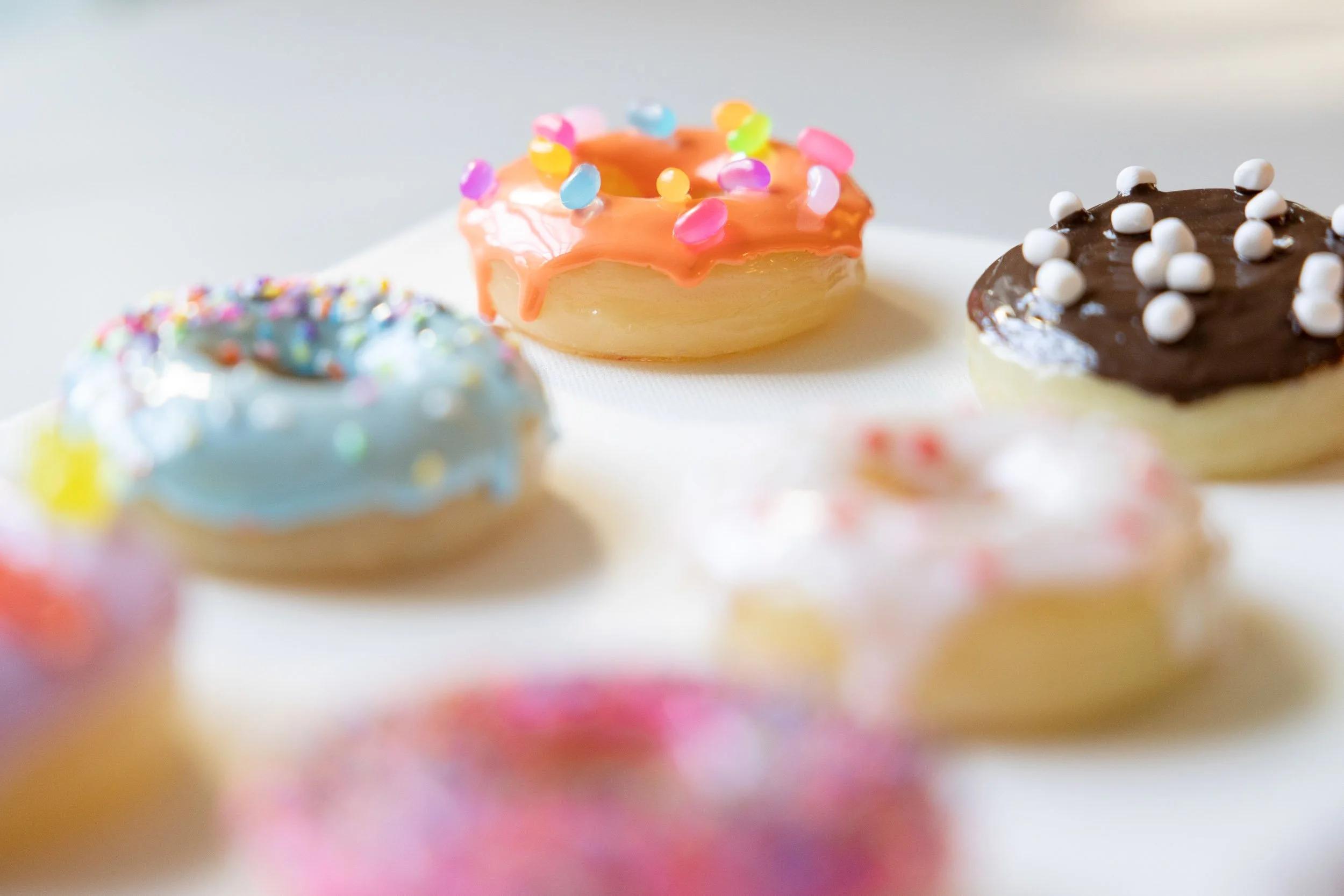 Assorted decorated resin donuts with colorful sprinkles, icing, and toppings on a white surface.