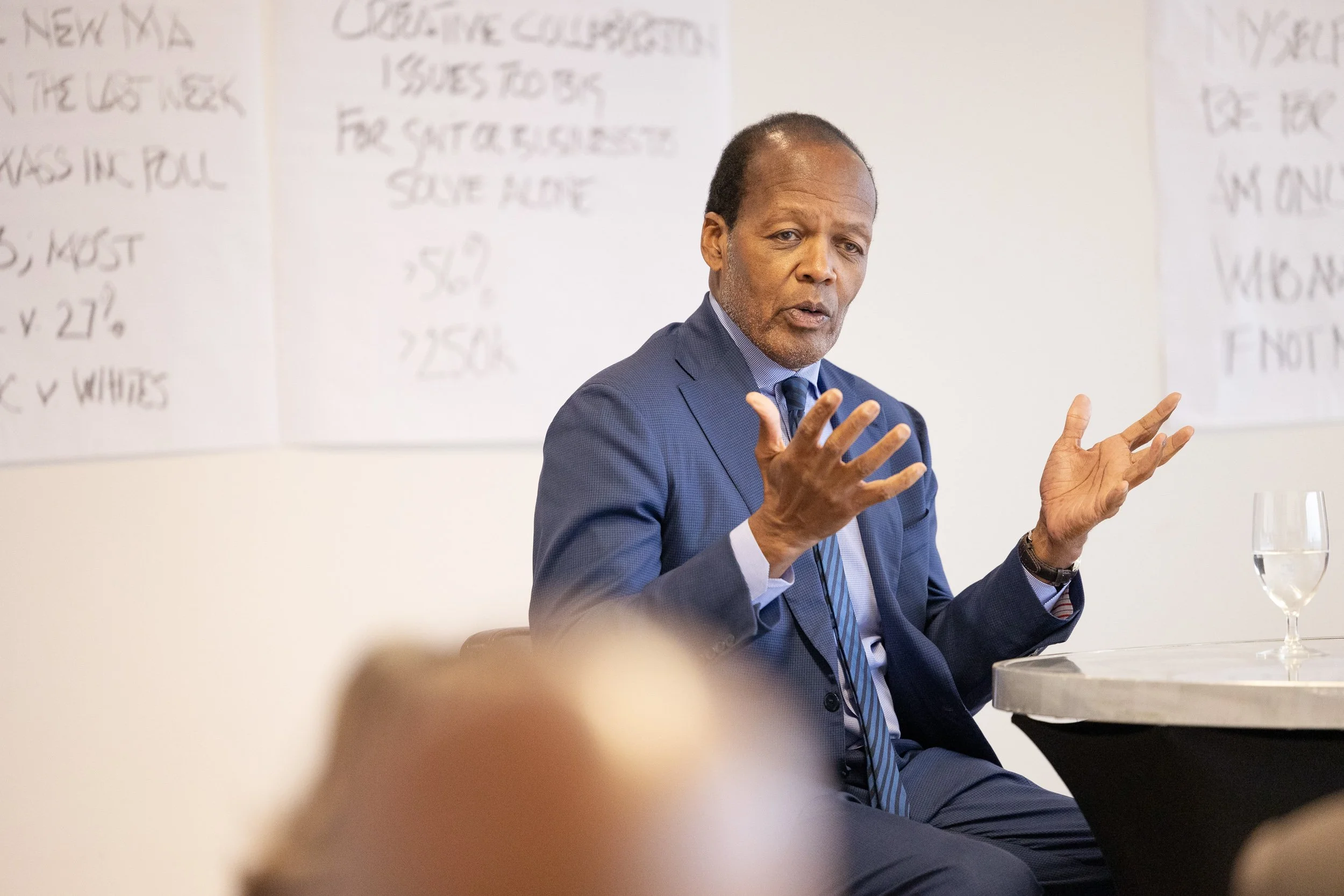 A man in a blue suit speaking at a Civic Action Project meeting in Boston.