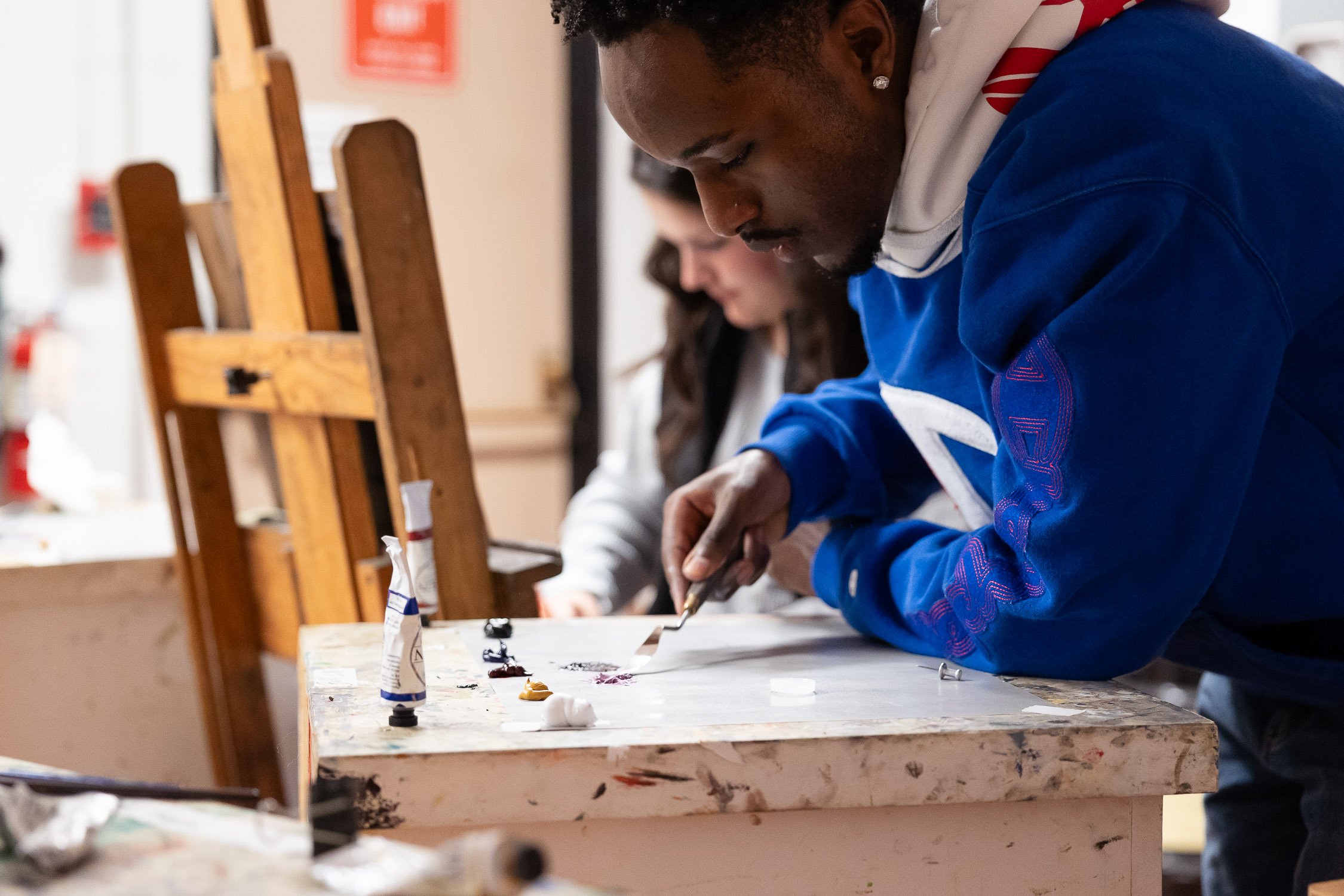 A young man painting on a canvas with a palette knife in a college art studio.