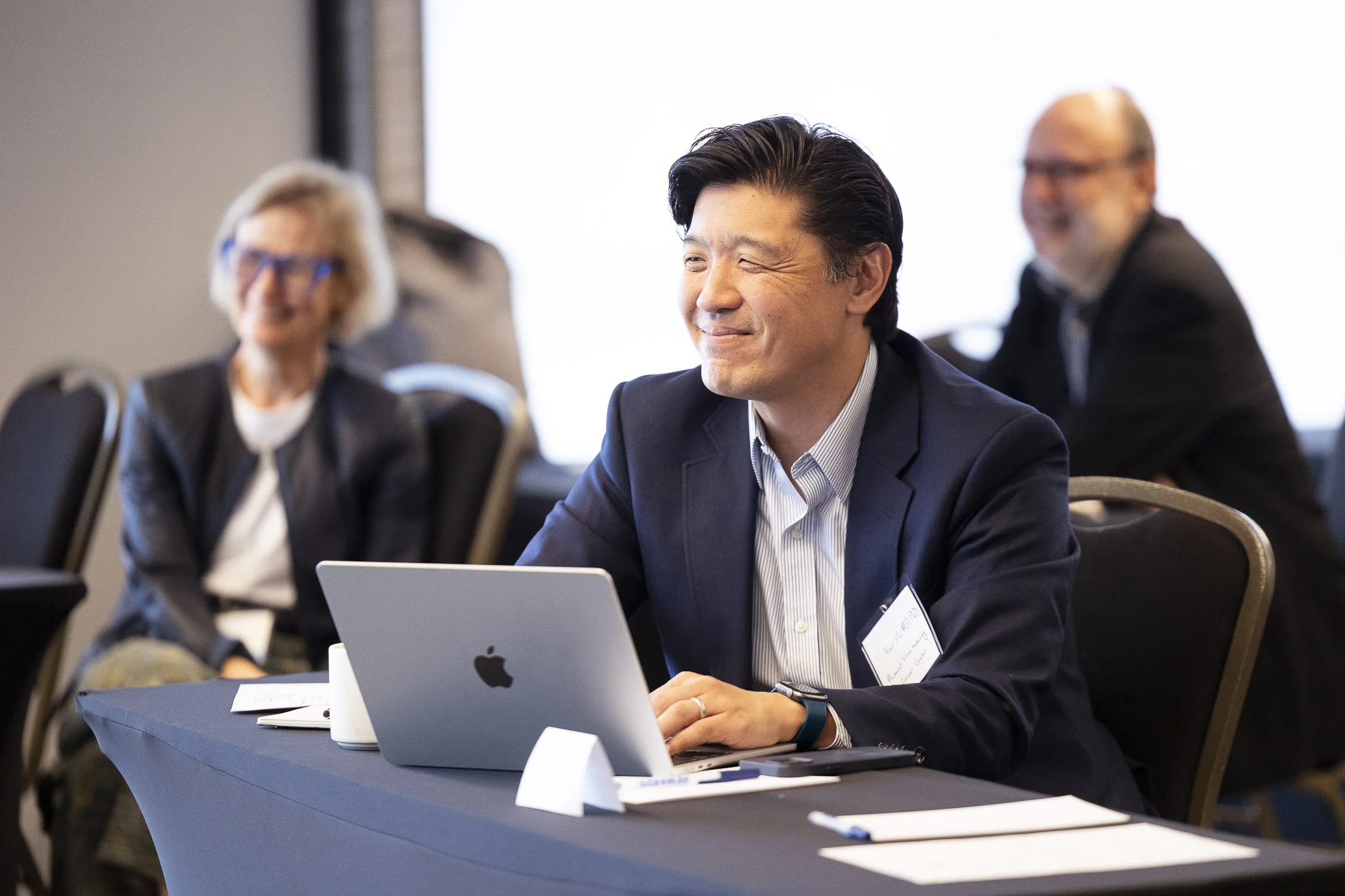 Man in a suit smiling at a laptop during a biotech conference at a hotel in Boston, Massachusetts.