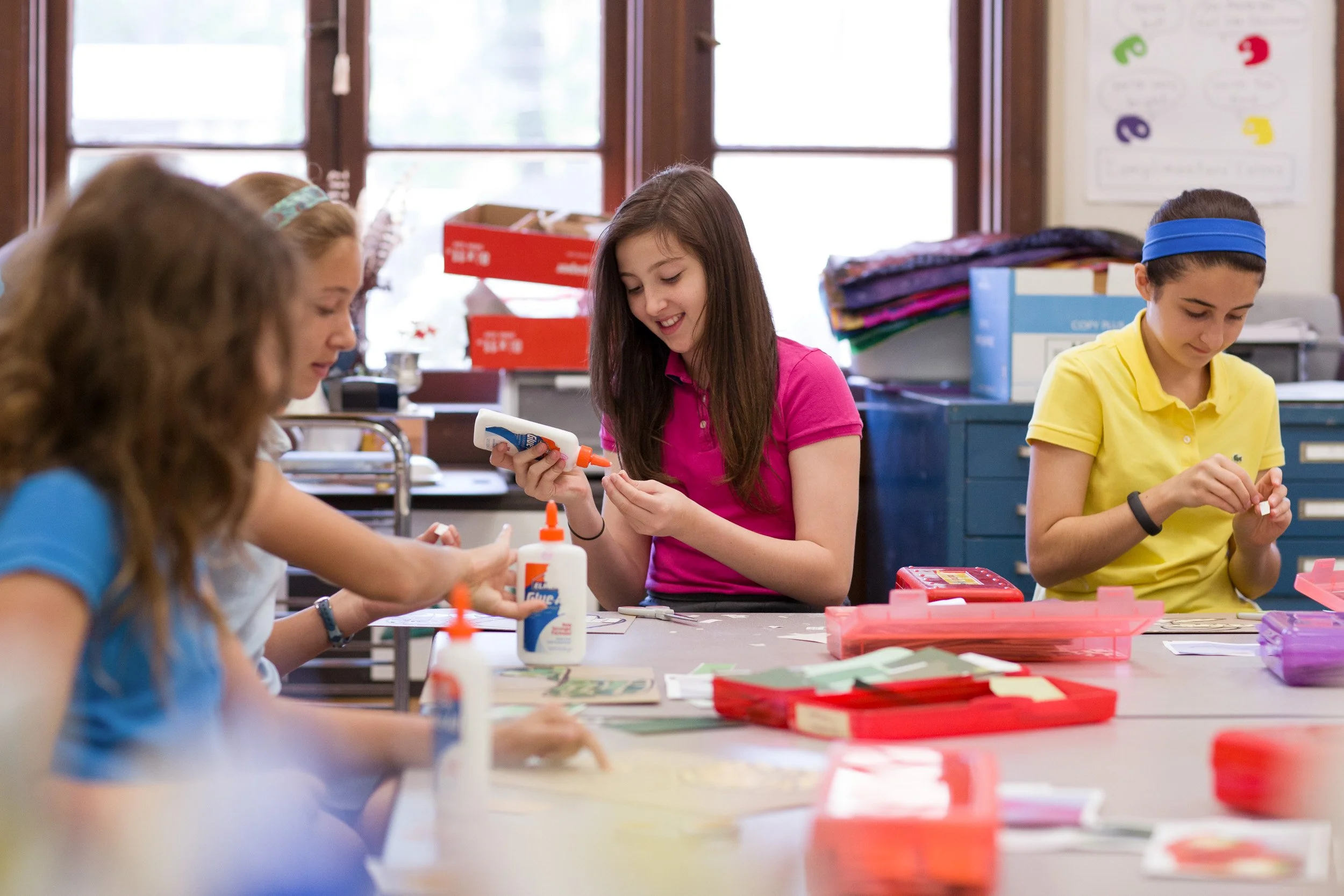 Four students sitting at a table in a classroom working on arts and crafts projects with glue and paper at Dexter Southfield school.