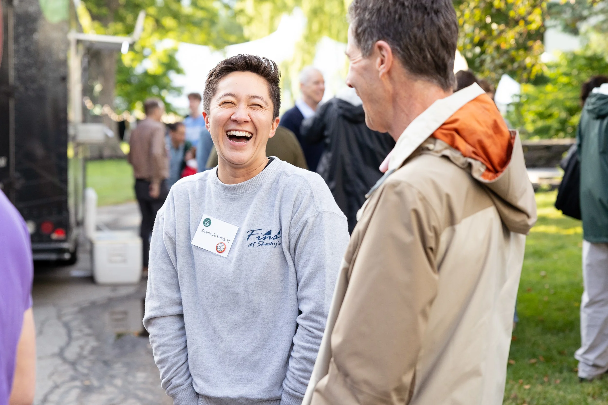 Two people laughing while talking outdoors at a high school reunion at Concord Academy.