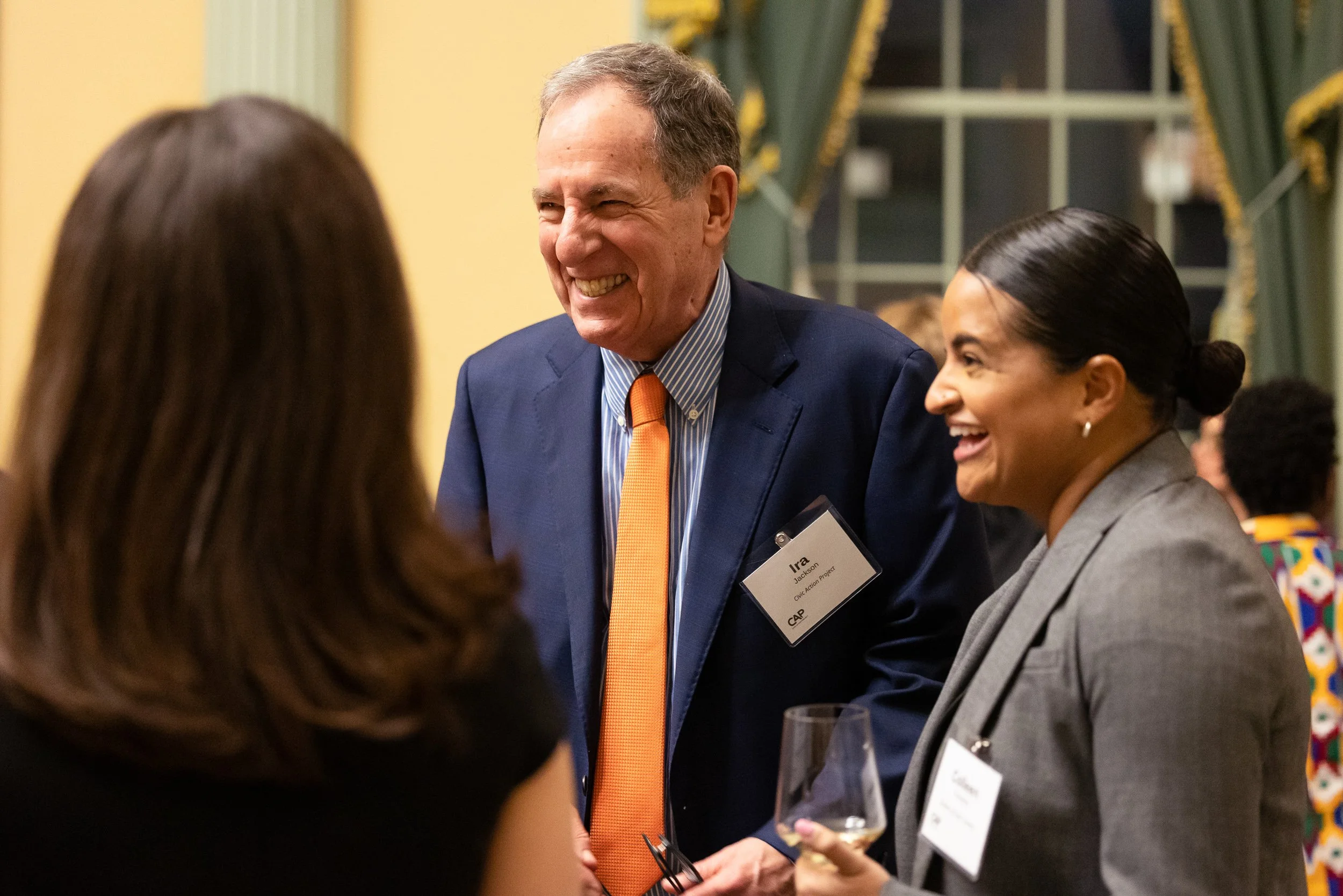Three people smiling and talking at a formal event at the Massachusetts State House in Boston.