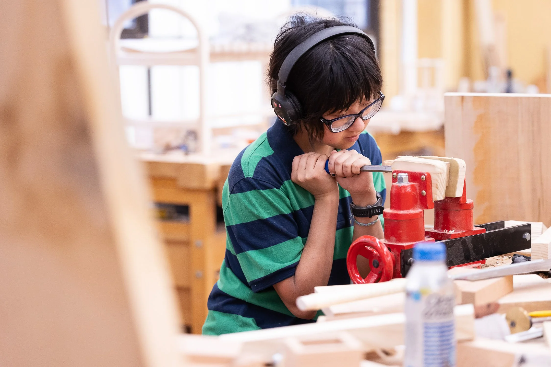 An art student using a hand drill on a piece of wood in a woodworking workshop.
