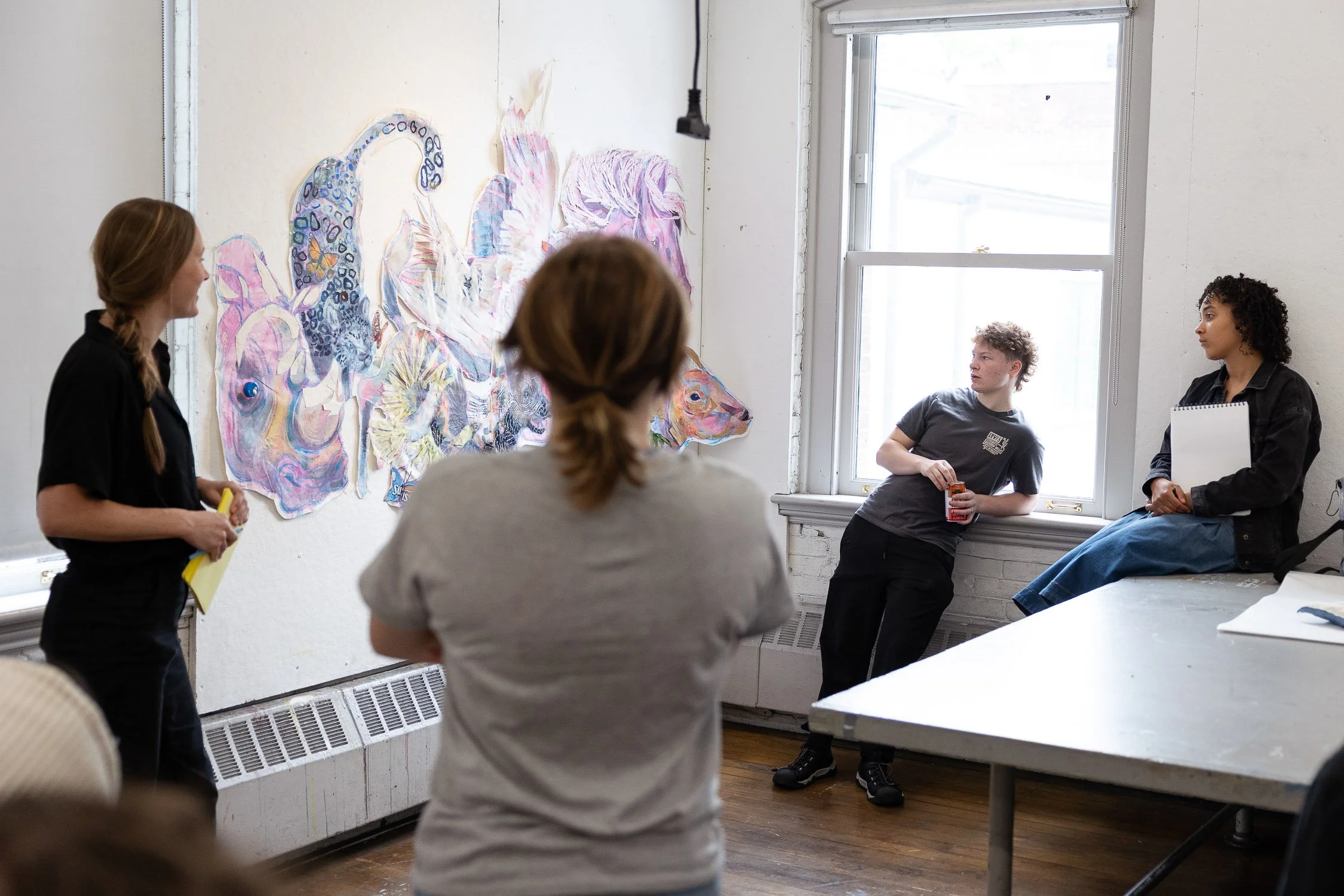 Group of students in an art classroom, looking at a colorful abstract mural on the wall.