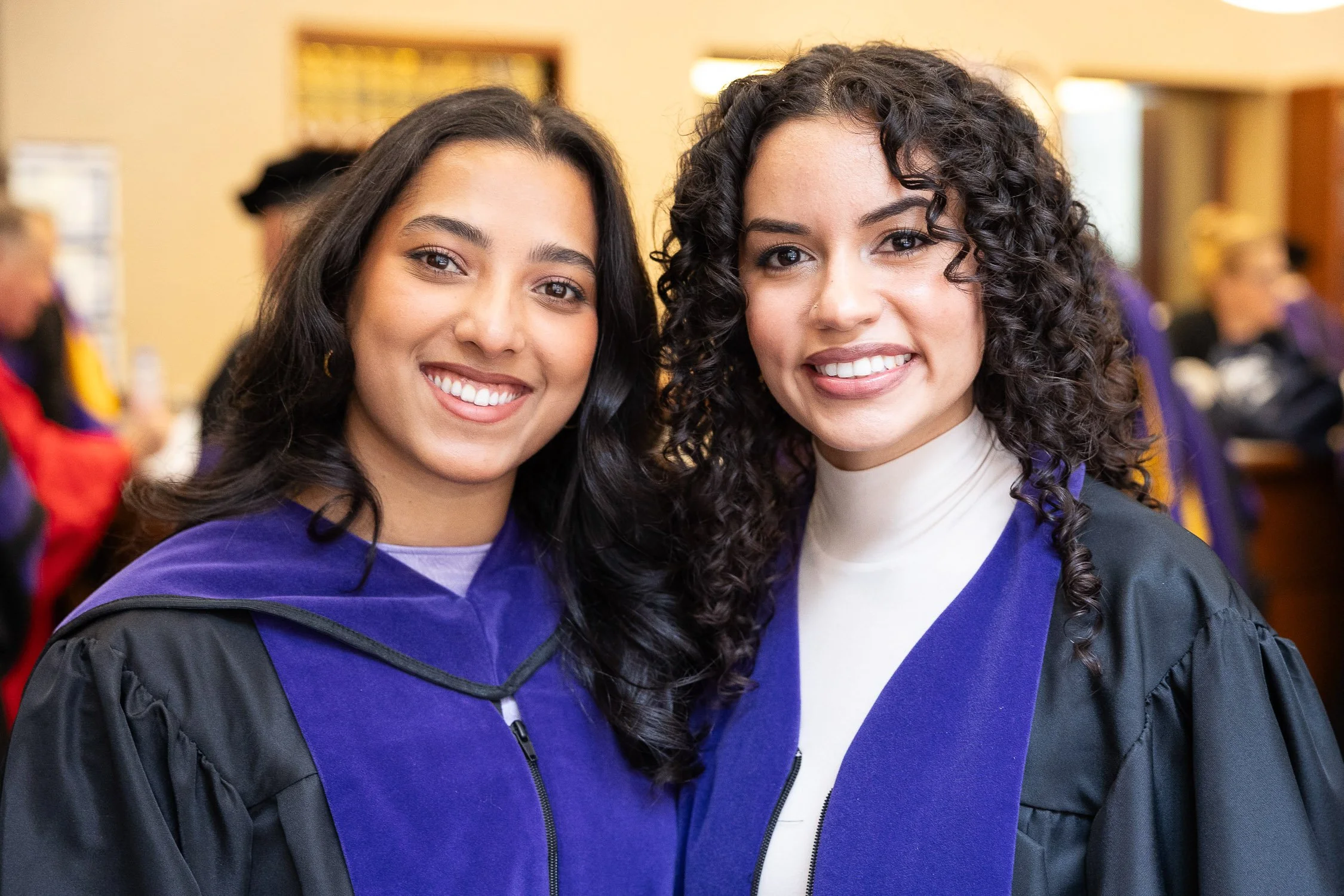Two young women in graduation robes smiling at the camera in law school library.