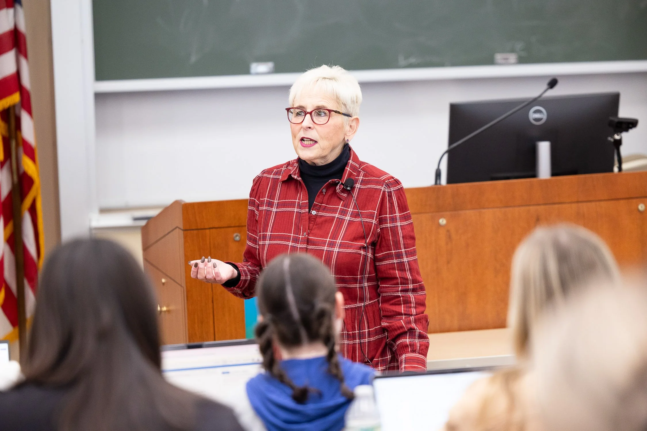 A woman is standing at the front of a classroom, speaking to students at a Boston college.