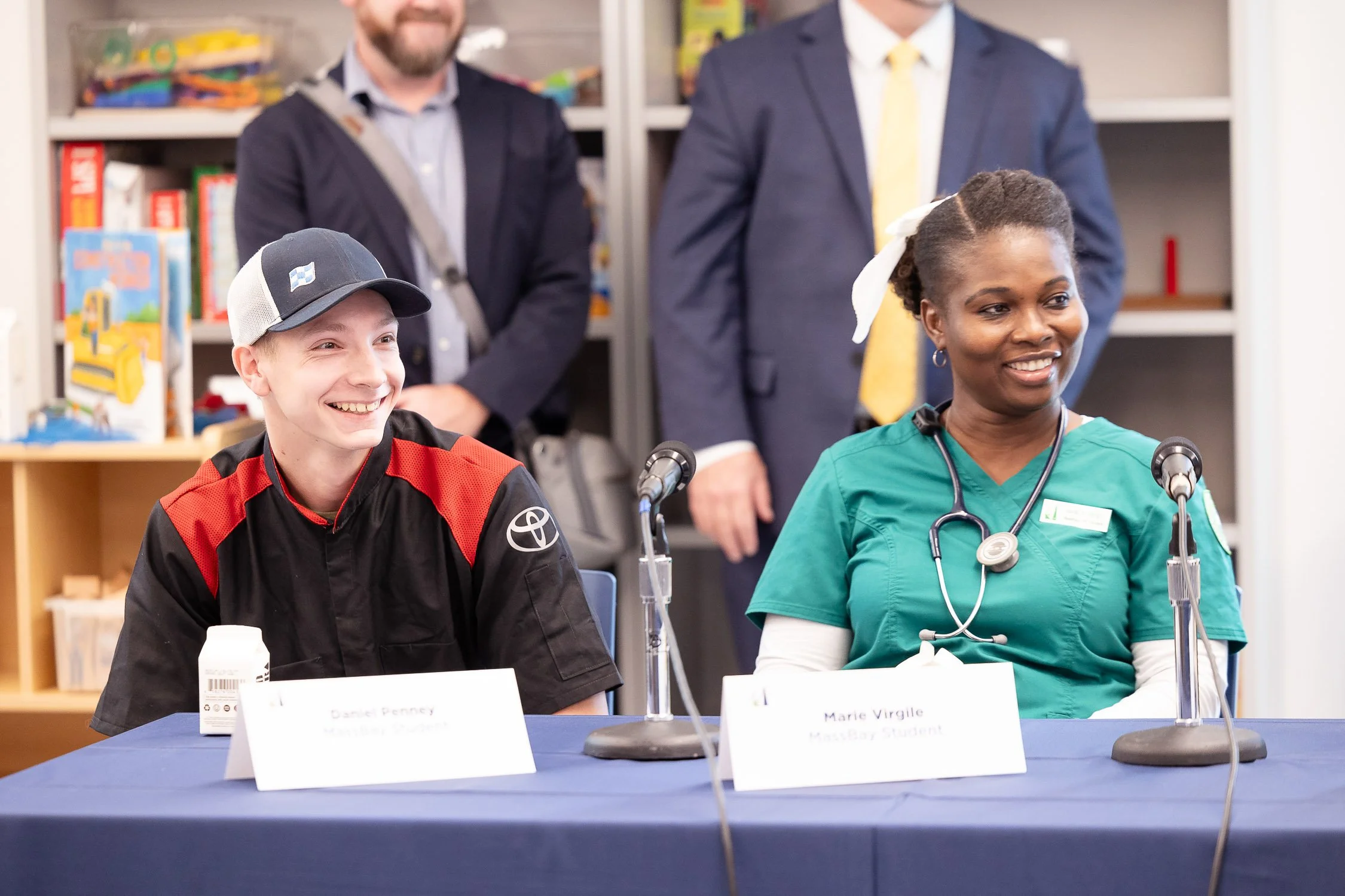 A young man sitting at a table with a nurse wearing scrubs and a stethoscope at a panel discussion at MassBay Community College in Framingham.