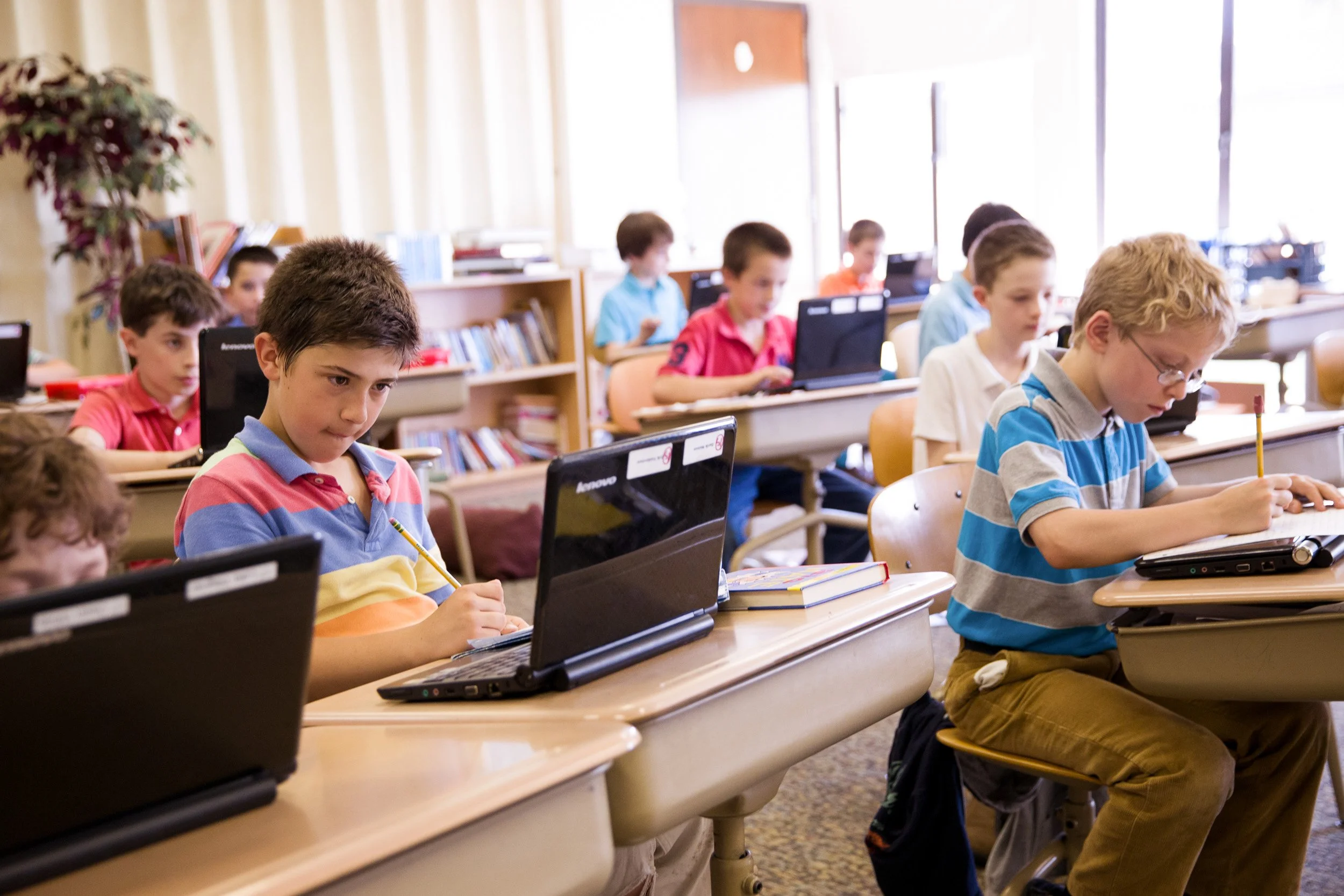 Classroom of elementary age students working on laptops at desks.