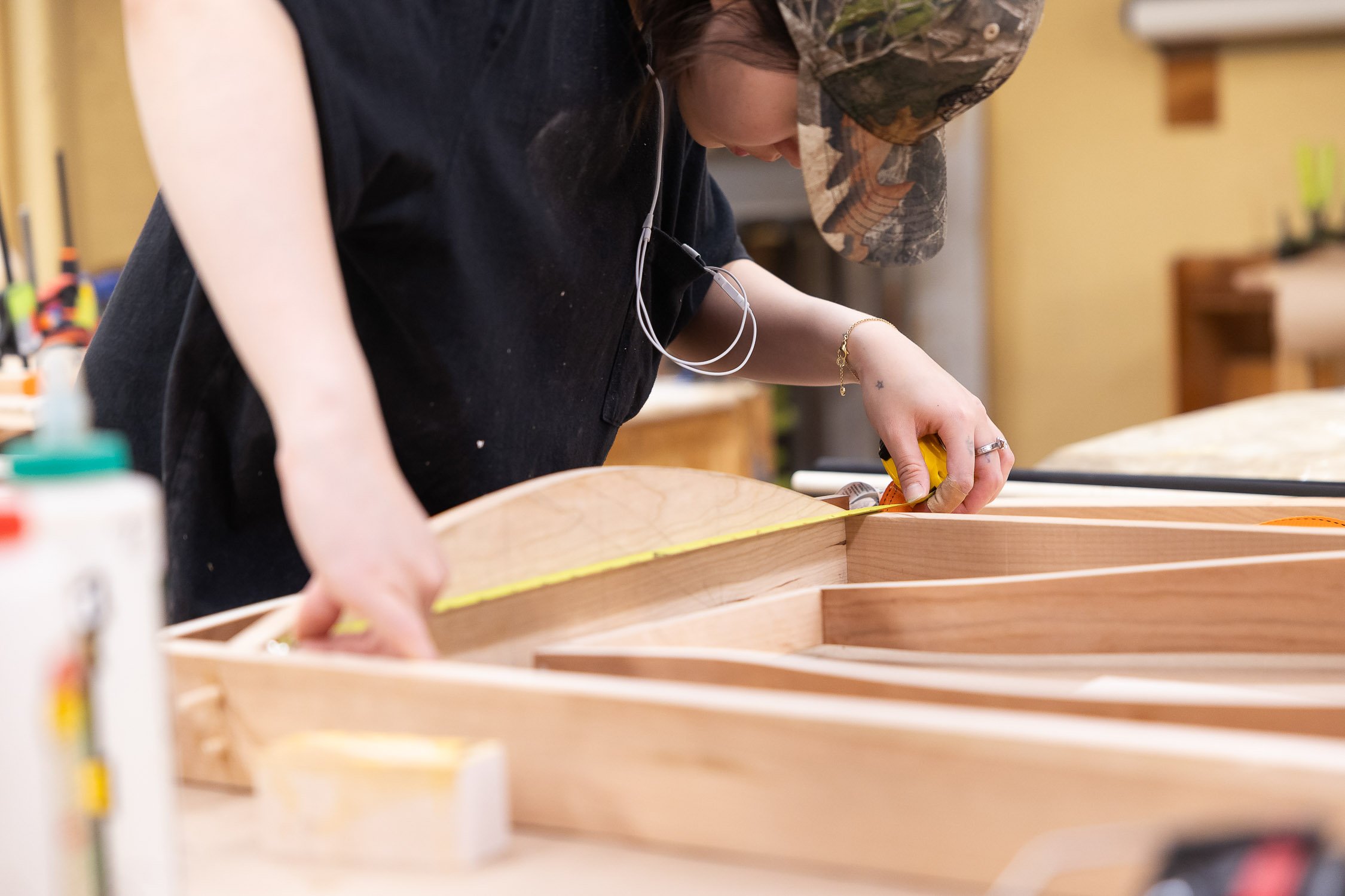 Person measuring wood pieces for a woodworking project in a college workshop.