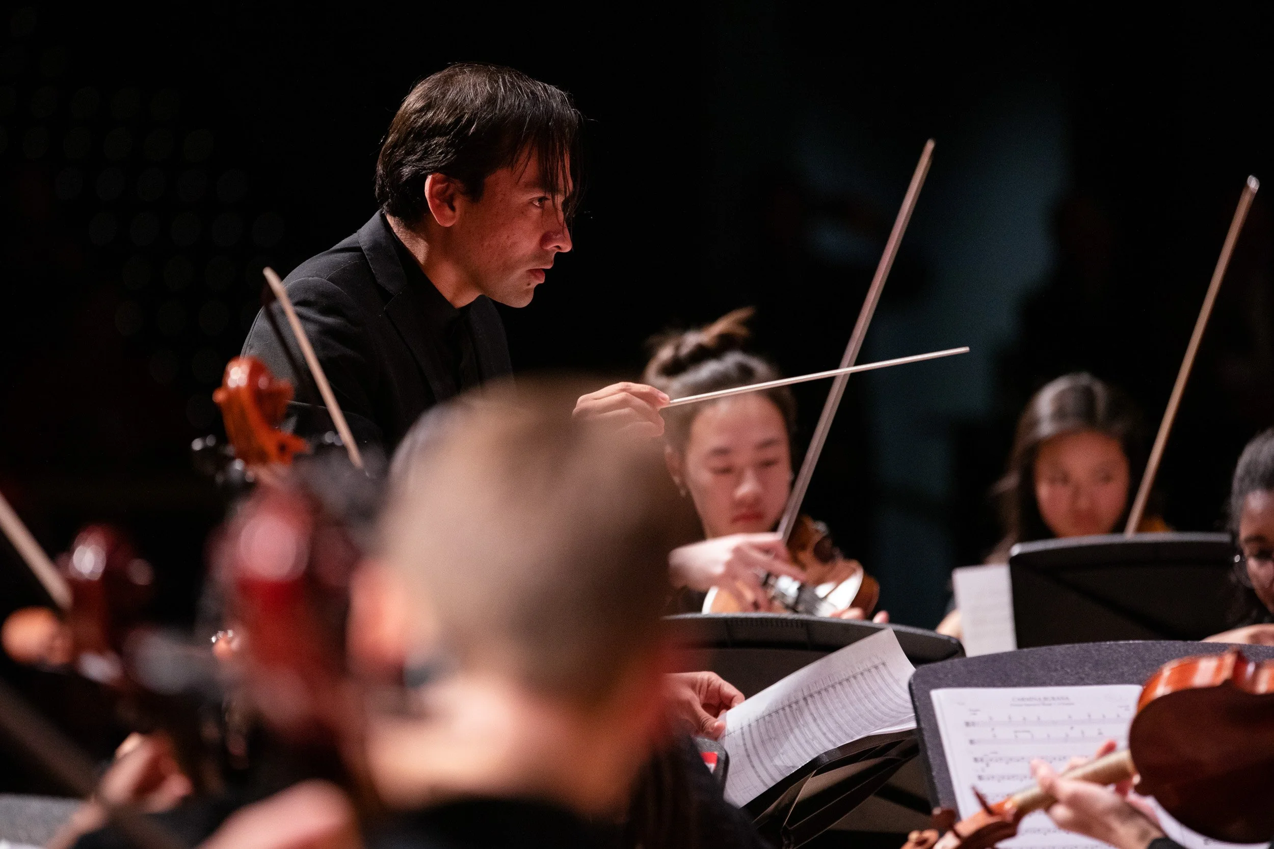 Orchestra conductor leading high school musicians during a performance at an independent school in Dedham, Massachusetts.