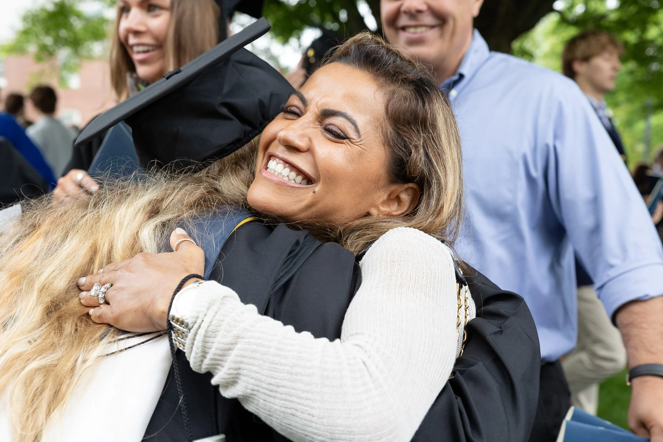 A woman in a graduation gown and cap hugging a woman after ceremony.
