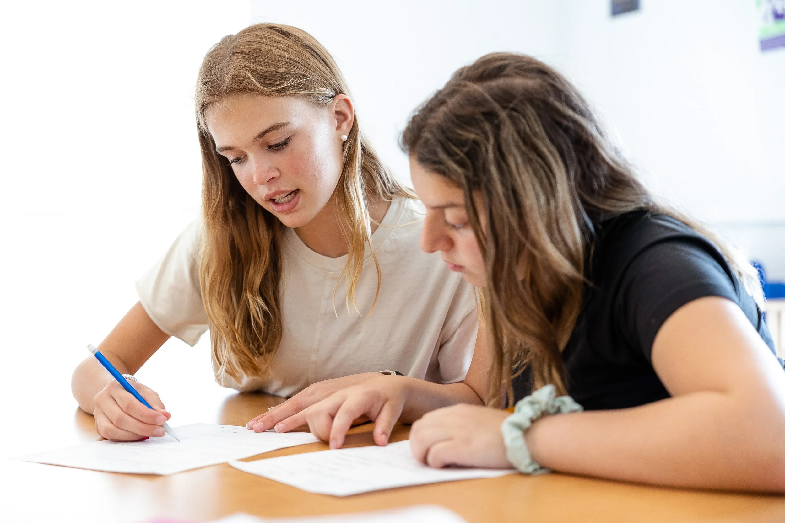 Two middle school students working on papers at a table in a classroom.