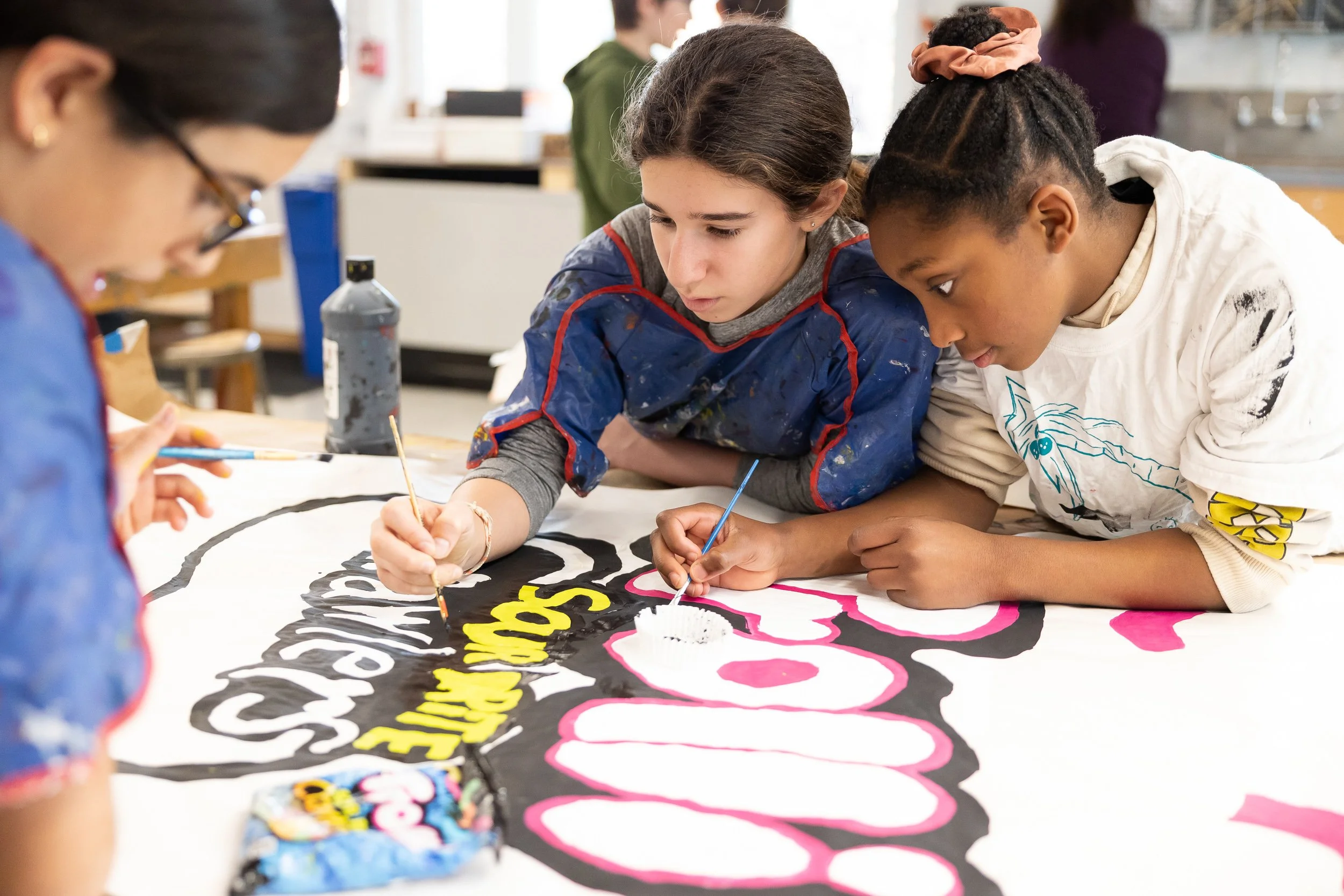 Three students painting a poster together as part of an art project in a middle school classroom.