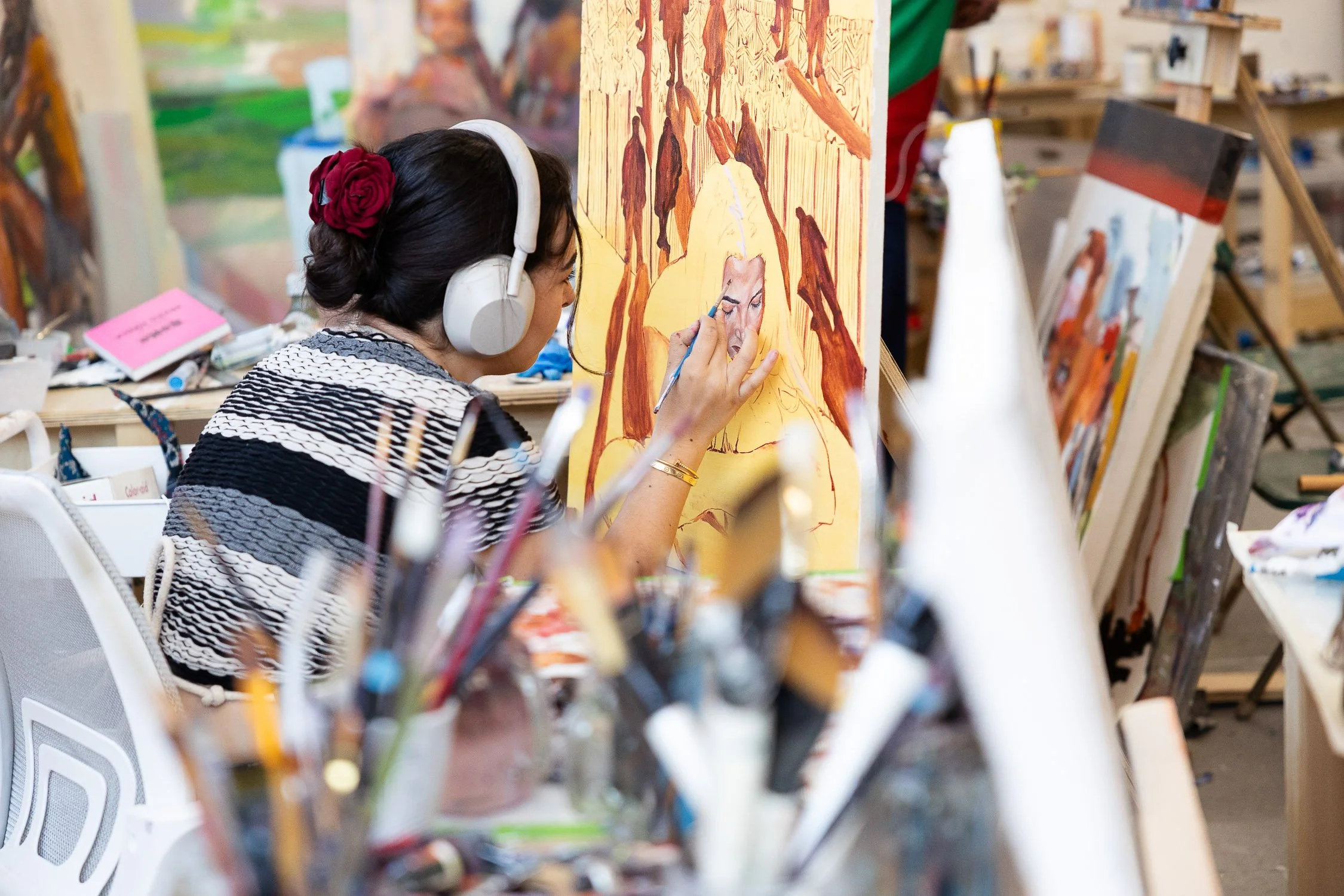 Student wearing headphones painting a portrait on a large canvas in an college art studio.