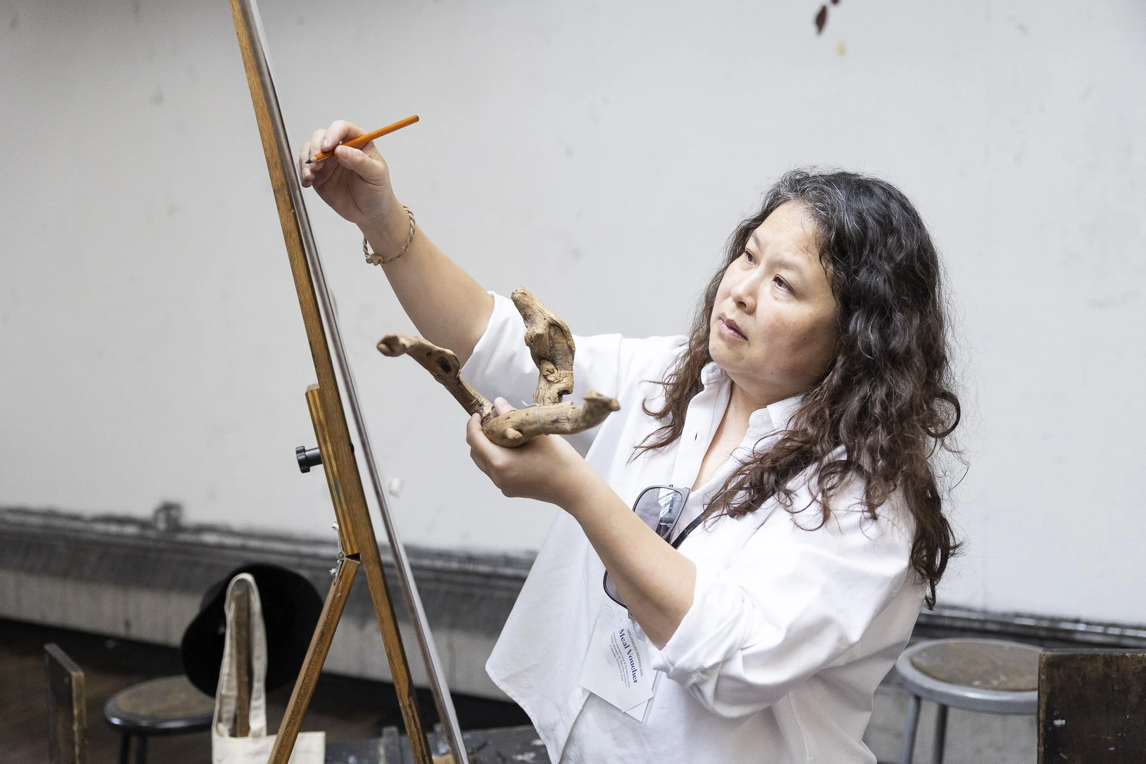 Woman holding a piece of antler in one hand and a pencil in the other, standing in front of an easel, engaged in sketching during a drawing workshop at RISD.