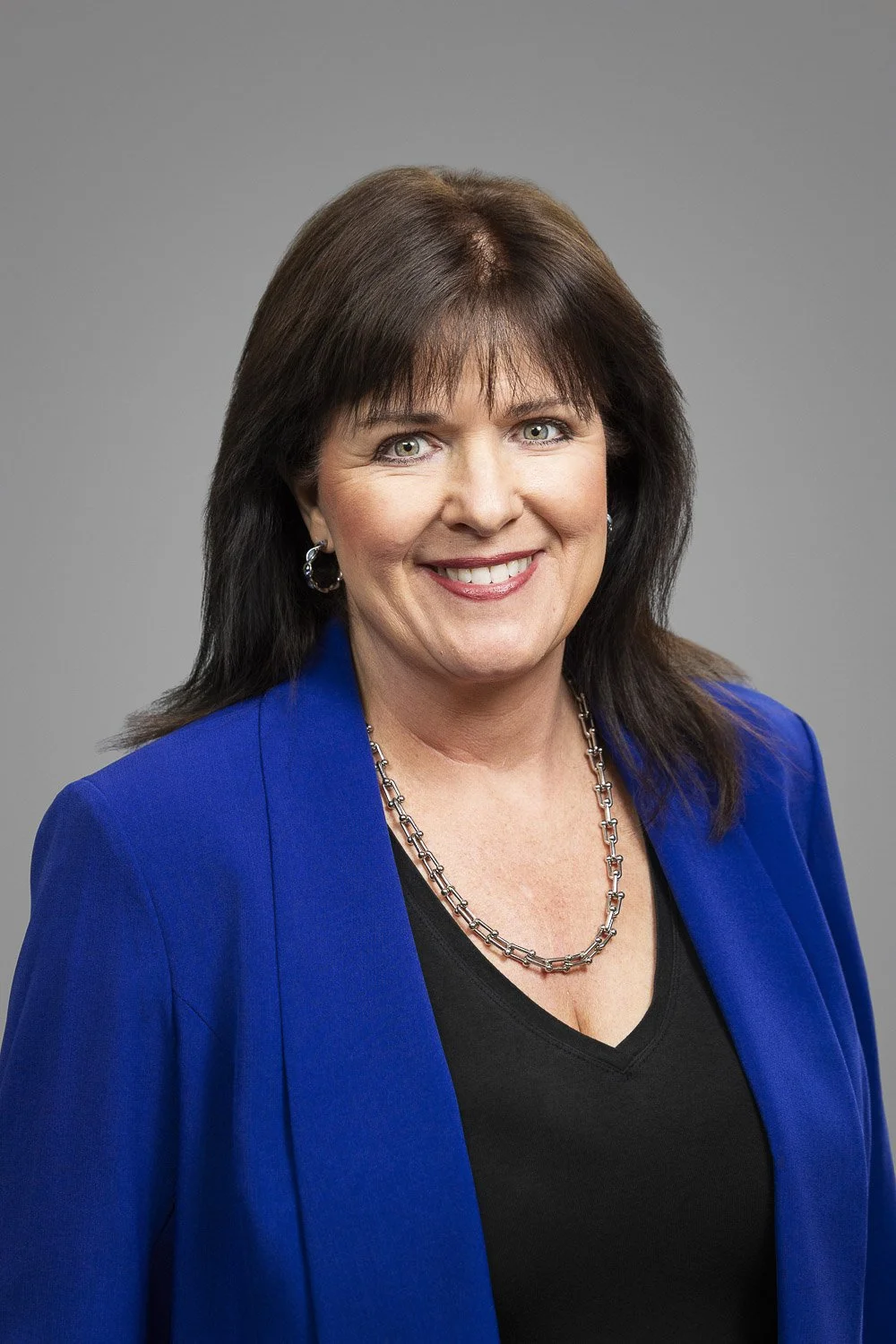 Portrait of a Boston law school professor with shoulder-length dark brown hair, wearing a blue blazer, smiling against a gray background.