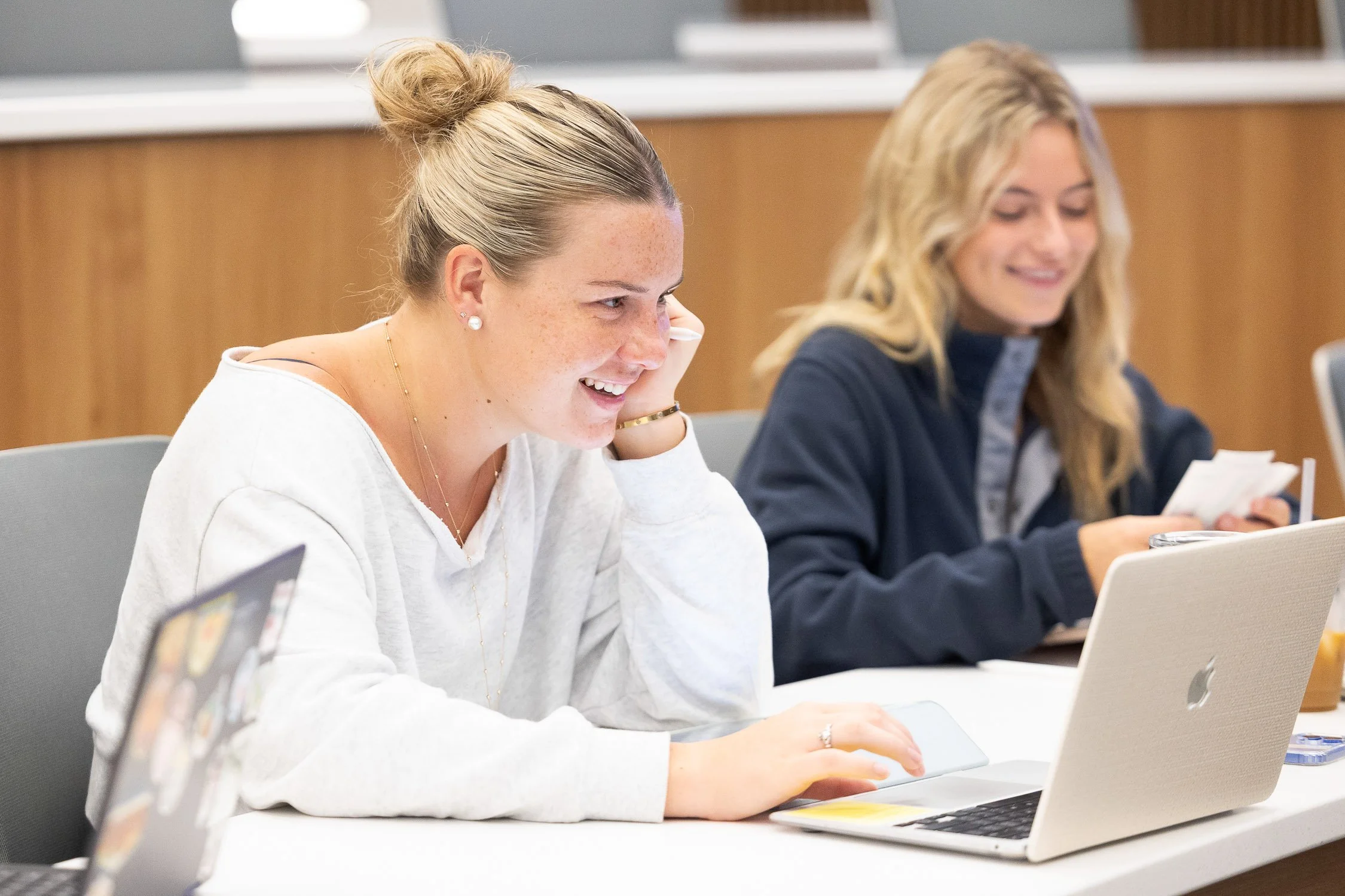Two young women sitting in a lecture hall working on laptops and taking notes at Saint Anselm College.