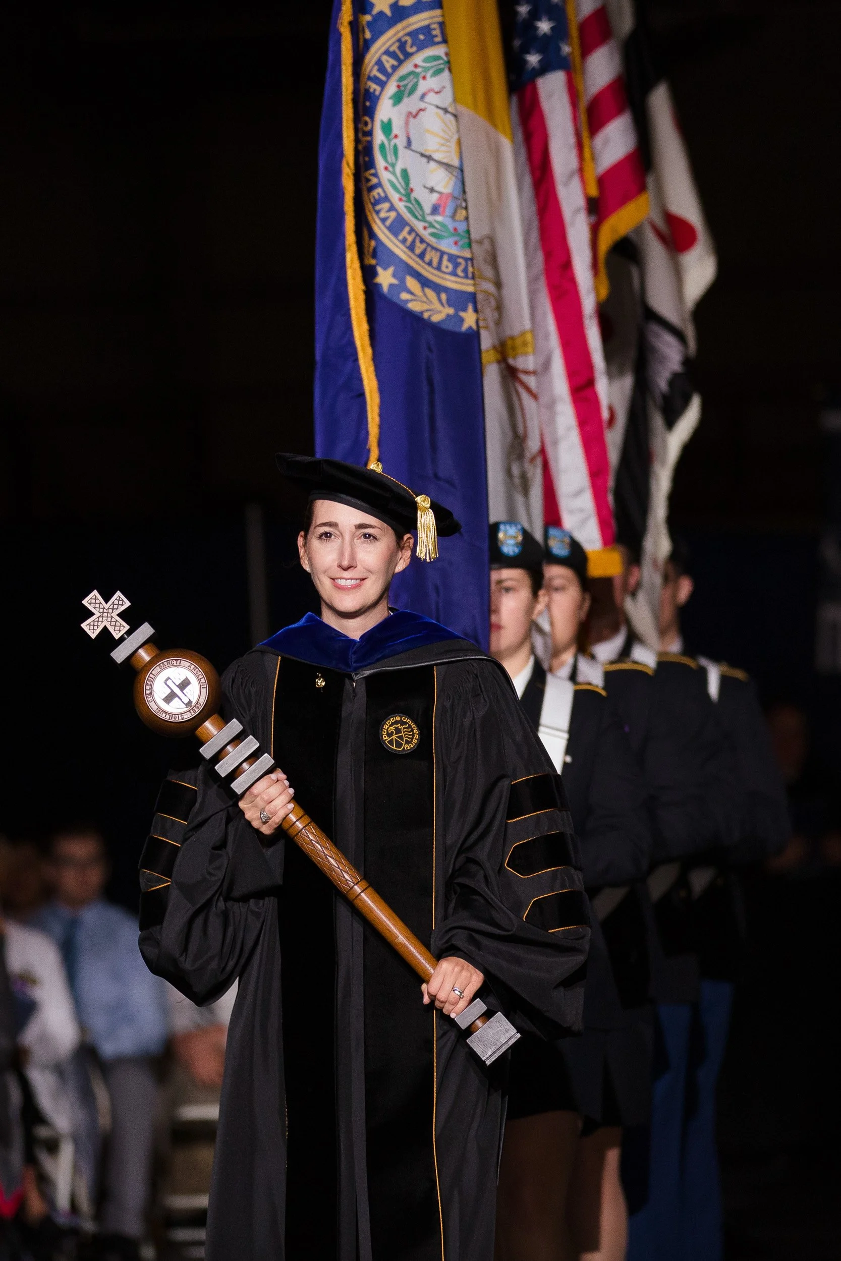 A woman in graduation ceremonial robes holding a ceremonial mace at a graduation event.