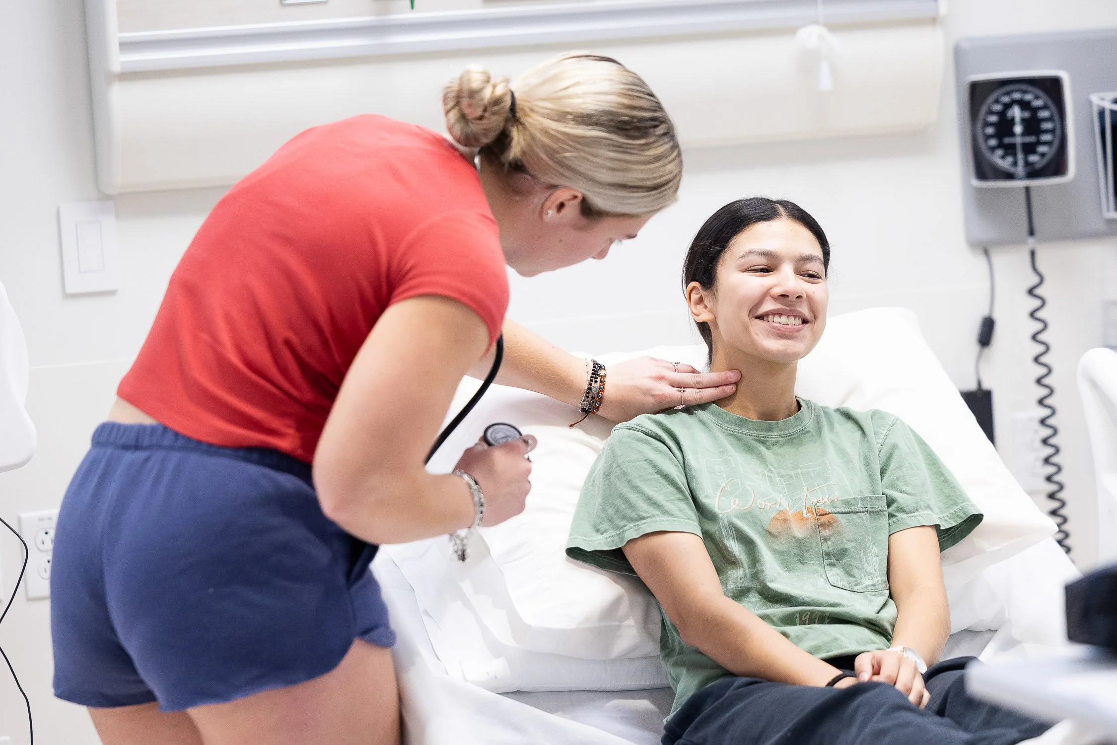 A student smiling while sitting on a hospital bed in a clinical simulation setting at a Massachusetts nursing program.
