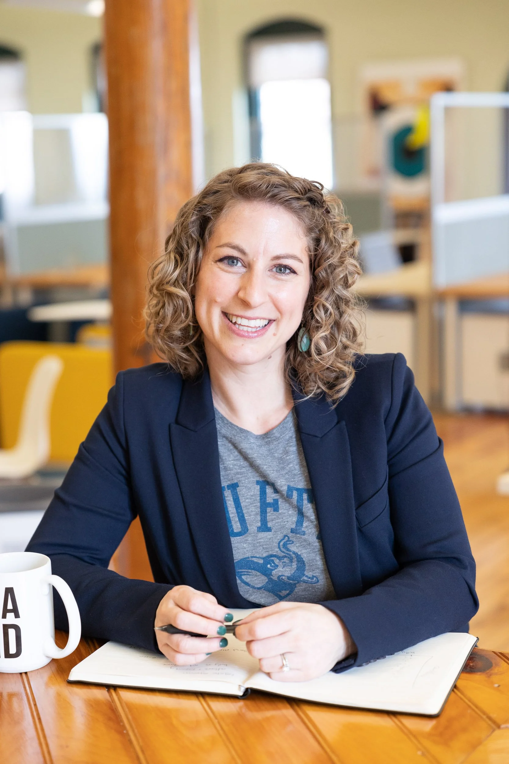 A female business owner wearing a blazer, sitting at a wooden table in a Massachusetts coworking space.
