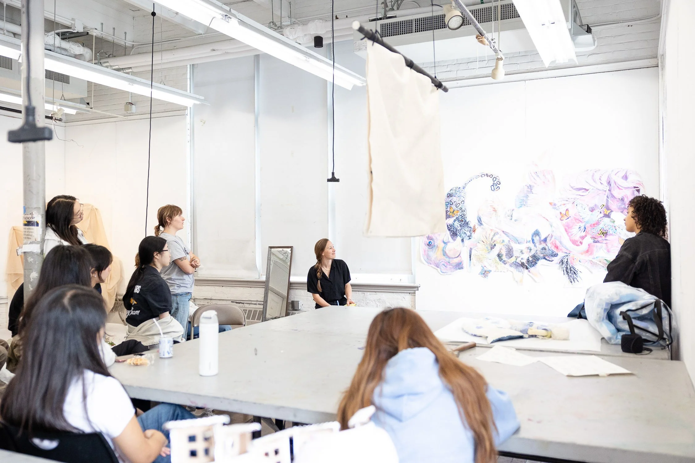 A group of students watching an instructor in an art classroom with colorful paintings on the wall at RISD.