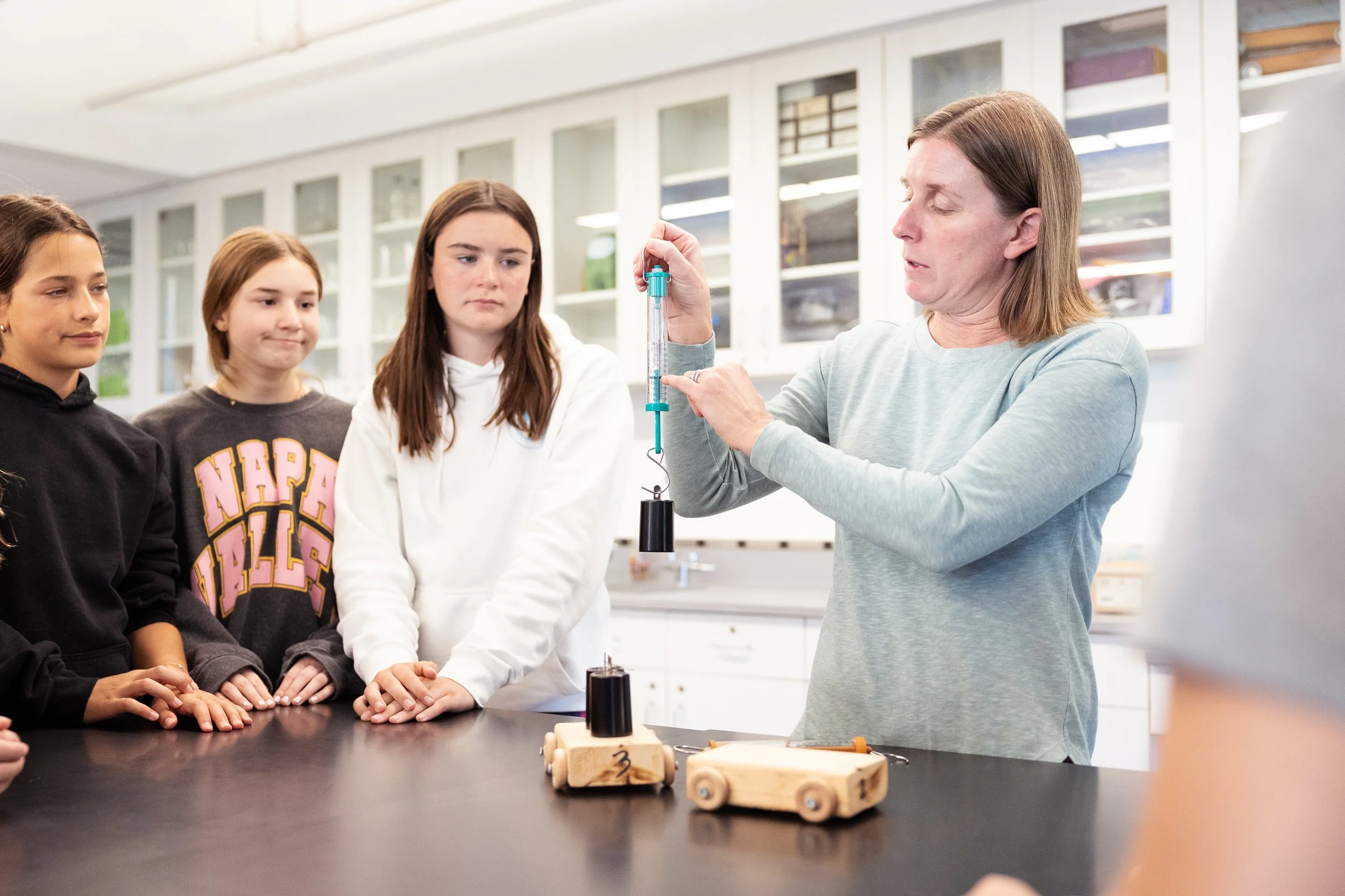 A teacher demonstrating a science experiment with a syringe to three students in a classroom.