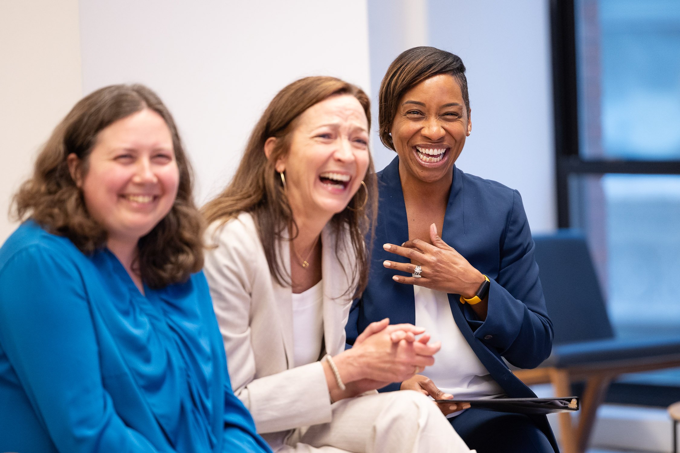 Three women, including Massachusetts Attorney General Andrea Campbell, sitting together and laughing at a nonprofit event in Boston.