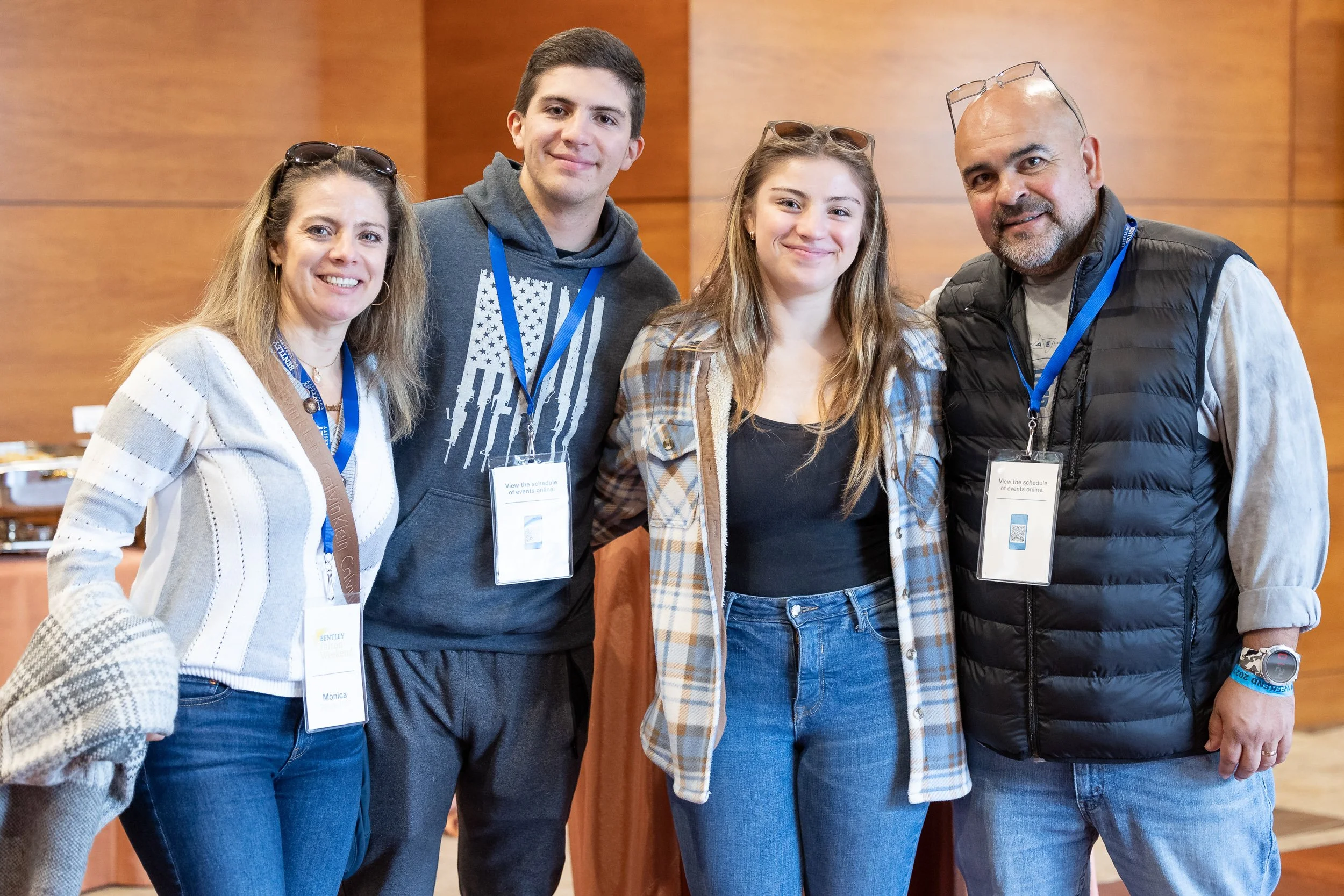 Four people standing together at an indoor reunion event at Bentley University.