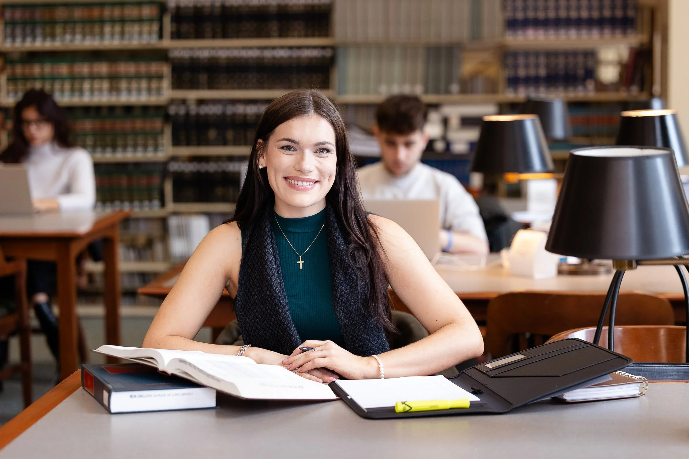 A woman smiling at a table in a library study room with books at New England Law Boston.