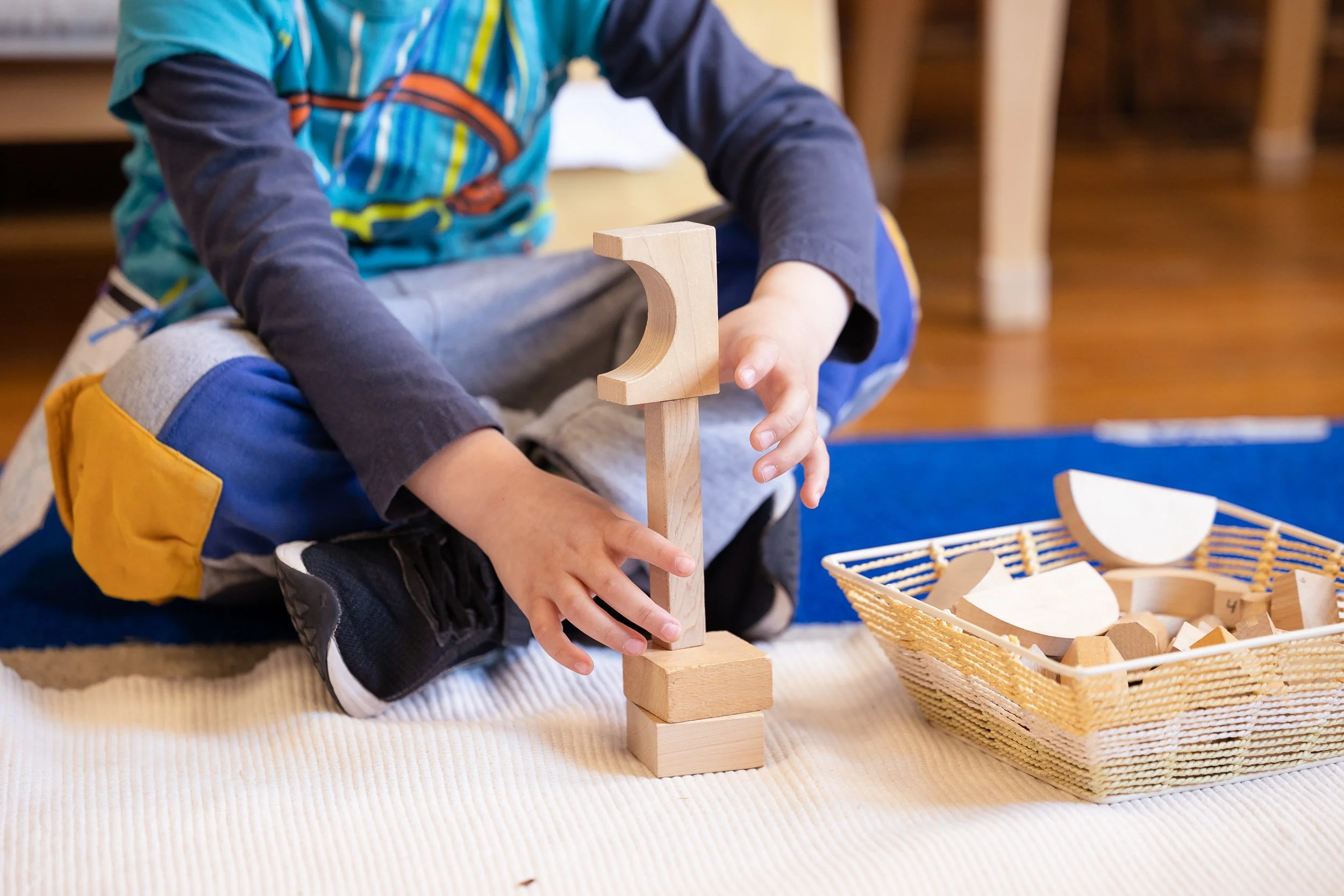 A child is sitting on the floor playing with wooden building blocks, stacking them to create a structure. 