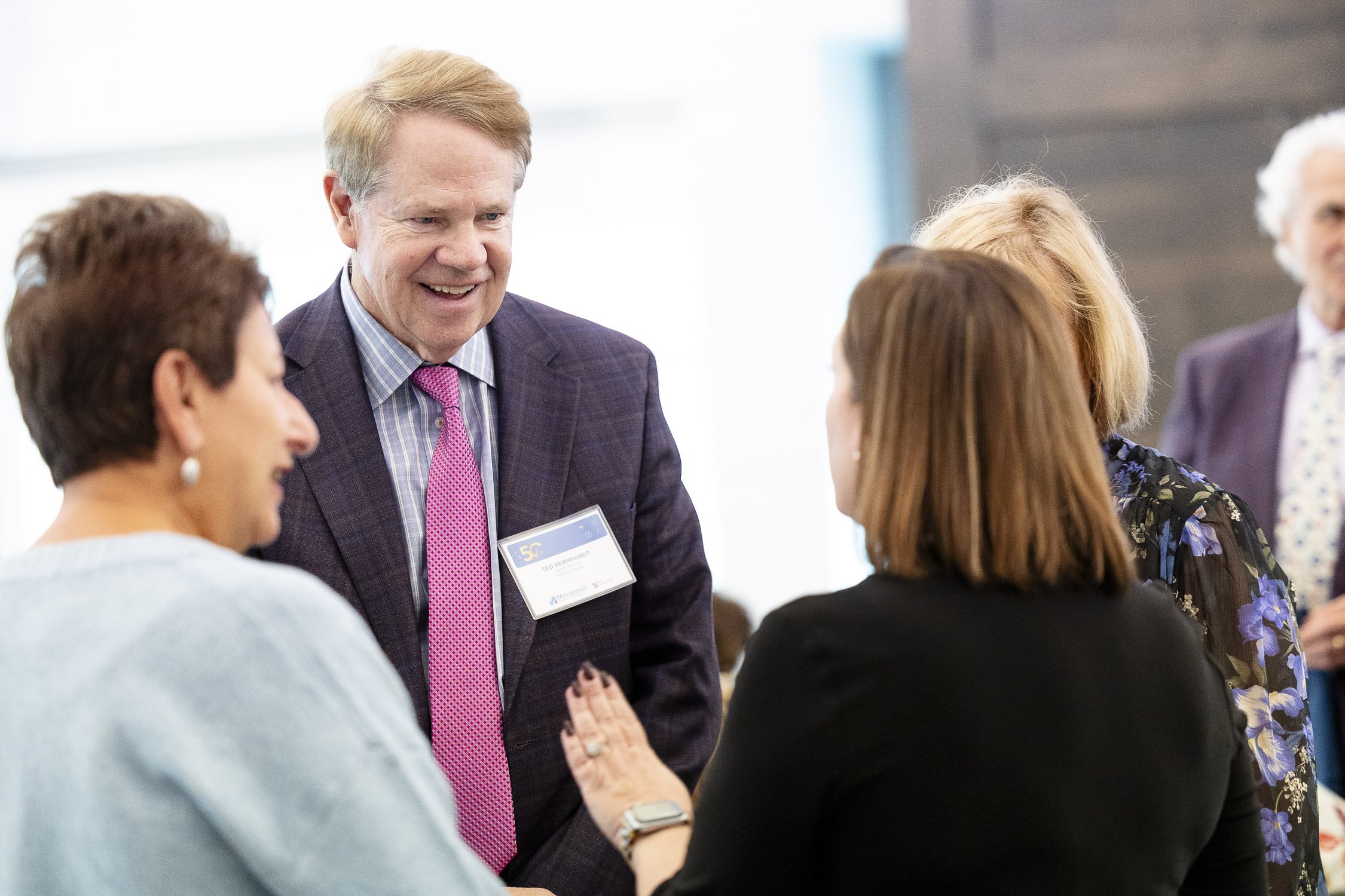 A group of professionally dressed people are smiling and engaging in conversation at a fundraising event in Boston.