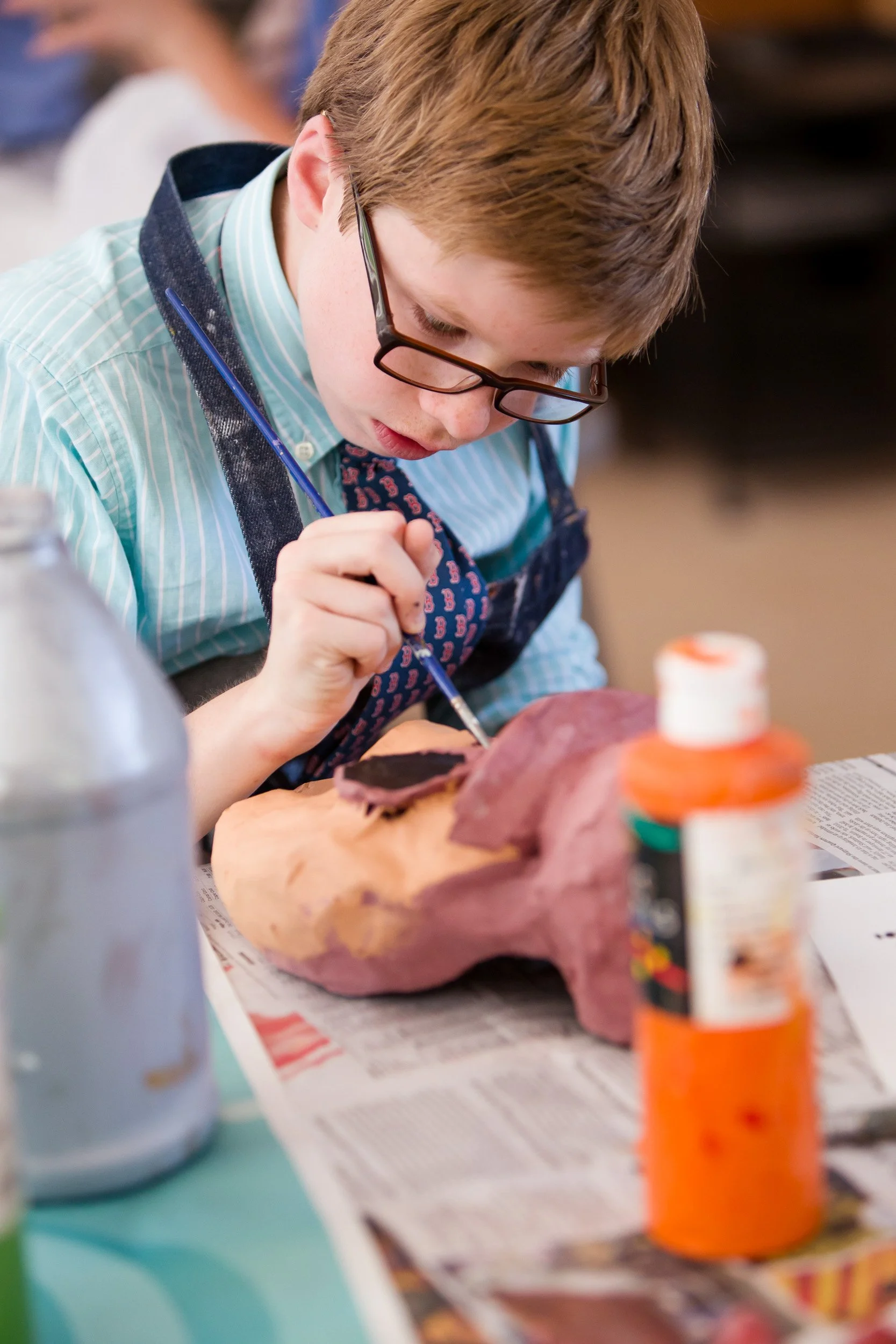 A young boy is painting a large sculpture in school art class.