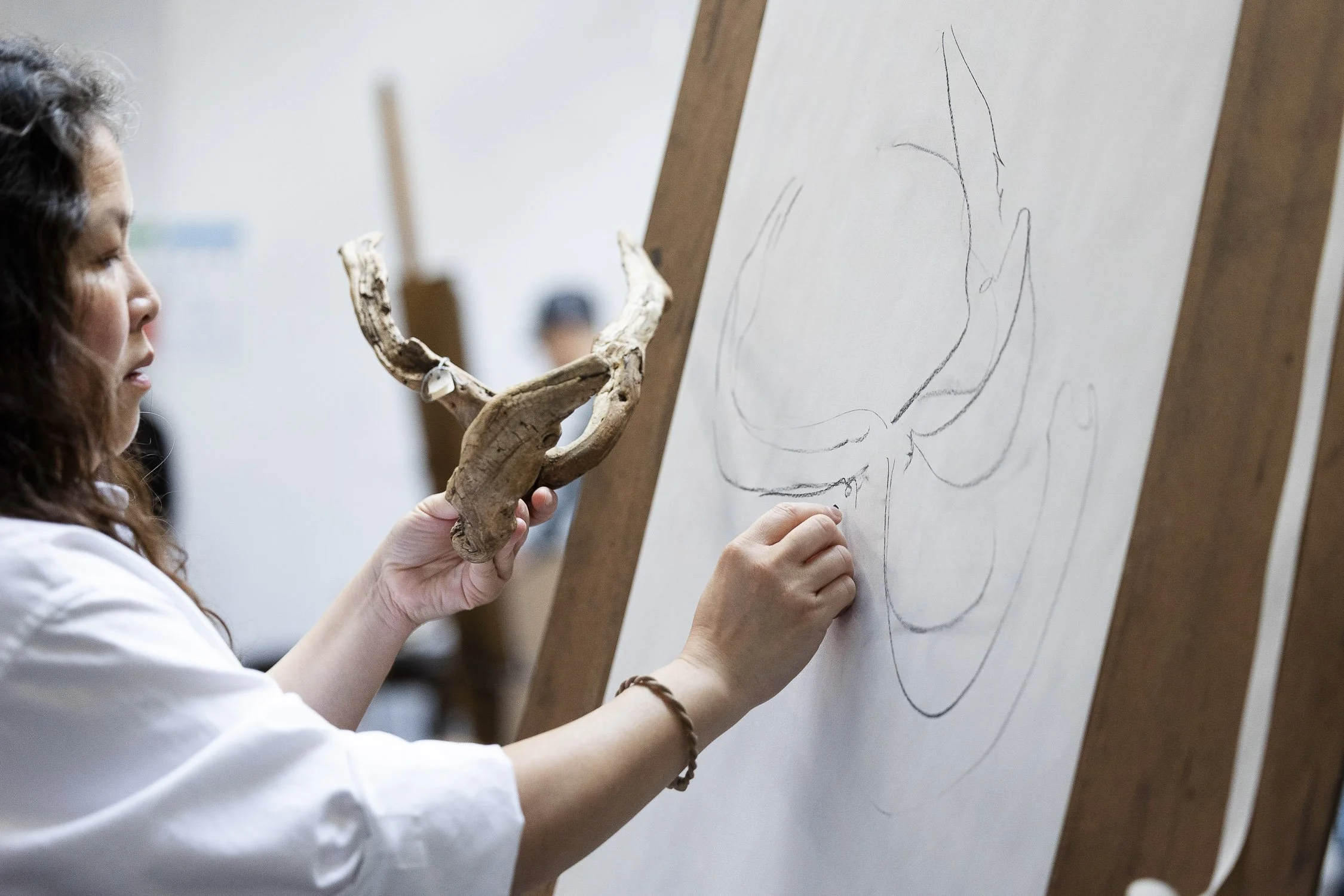 A woman drawing on a large sheet of paper on an easel, holding a piece of antler in her left hand.