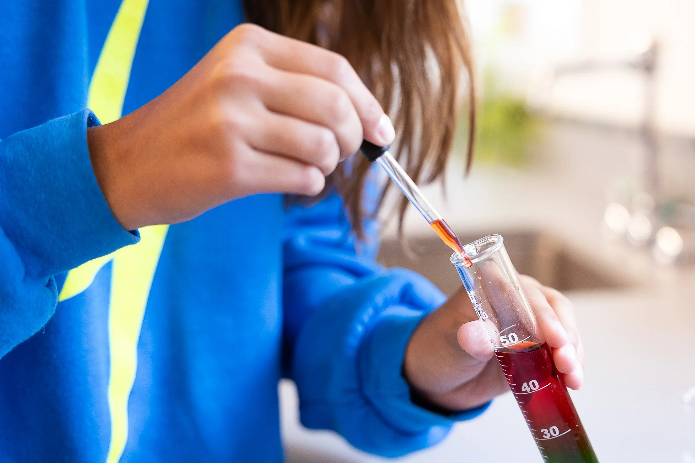 A middle school student holding a test tube with red liquid and using a pipette to transfer liquid into the test tube.