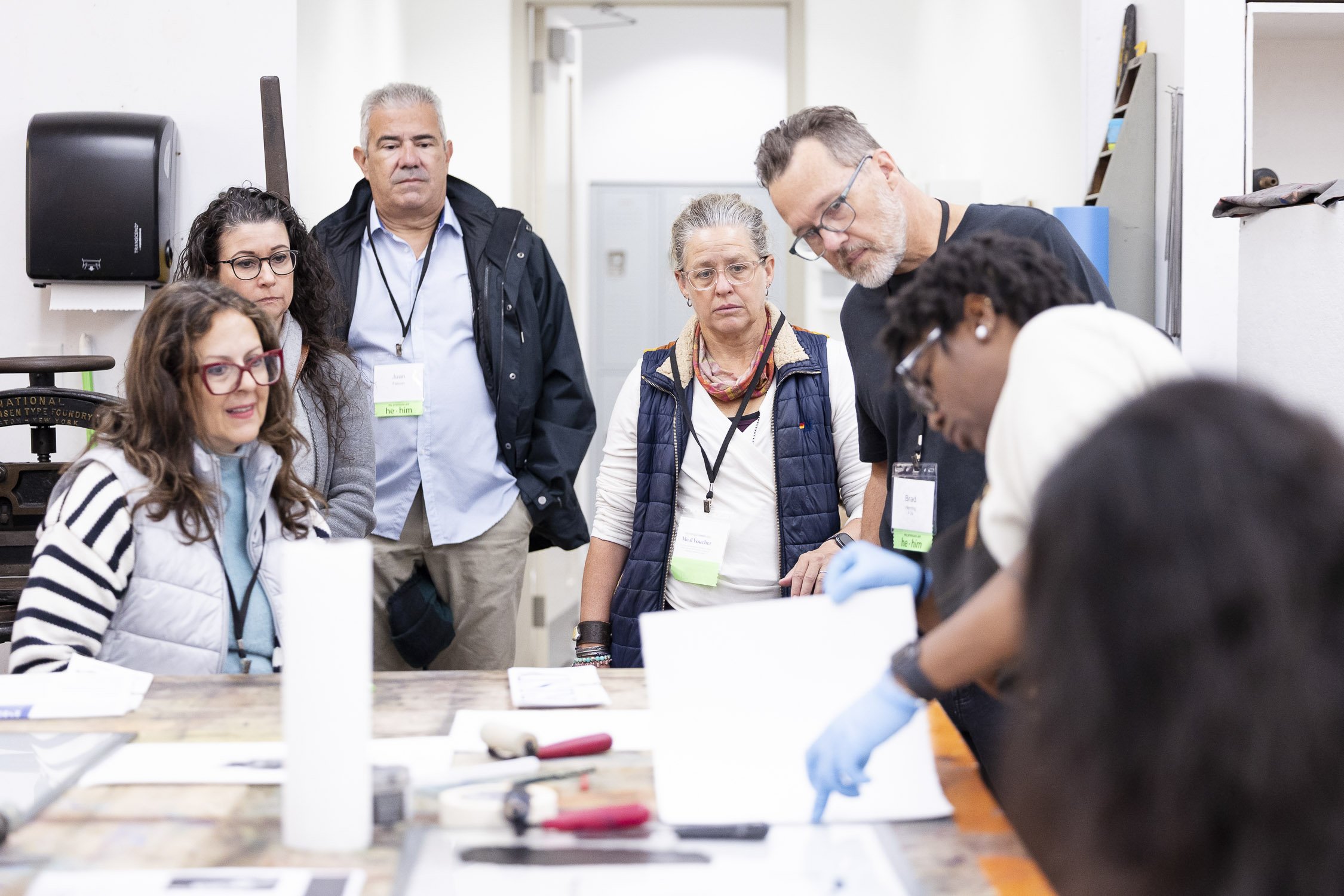 Group of people observing a demonstration with a person handling printmaking tools at a RISD workshop.