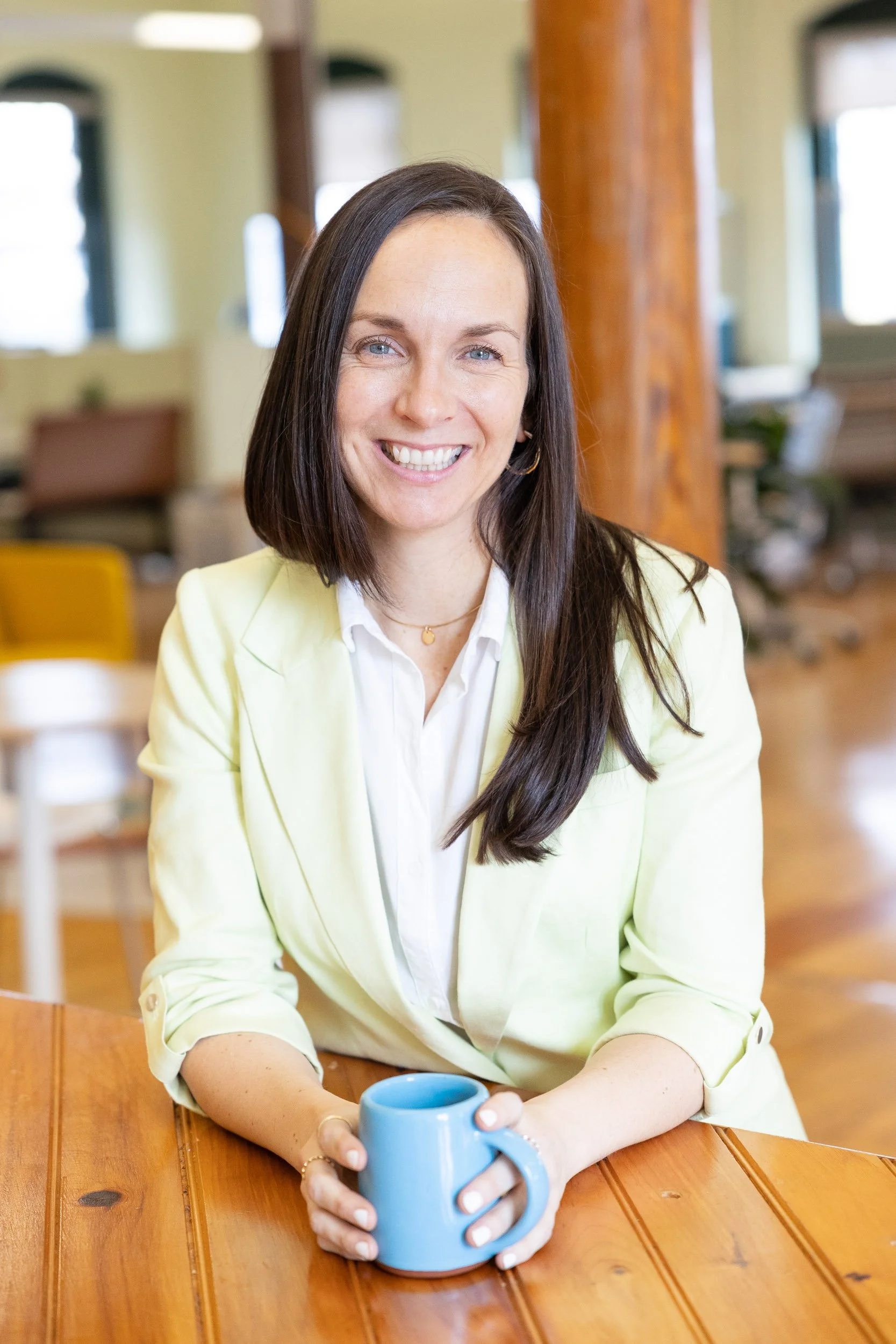 A female business owner wearing a light yellow blazer at a coworking space in Massachusetts.