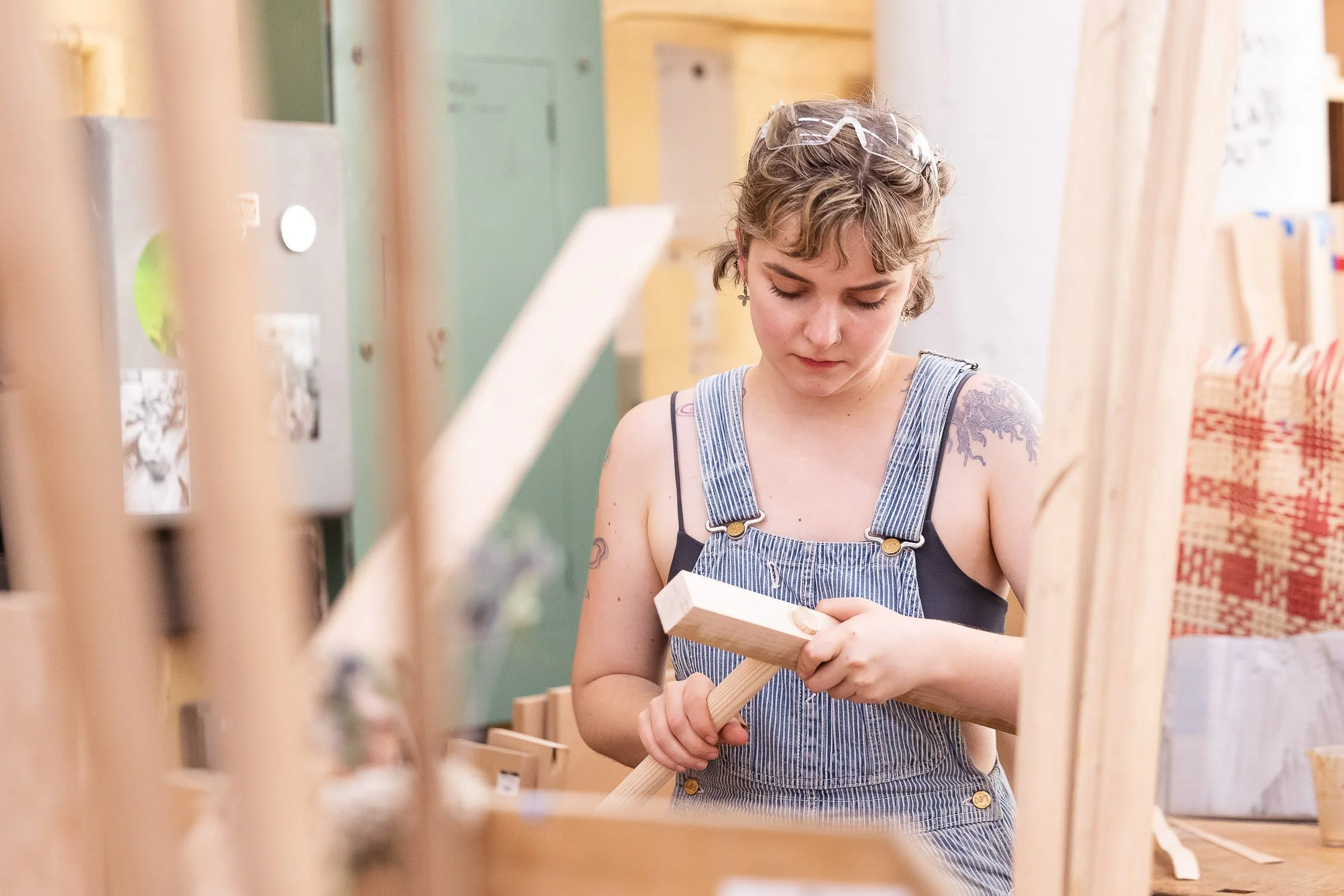 A female student working in a college woodworking shop, sand shaping a piece of wood with a hammer and chisel.