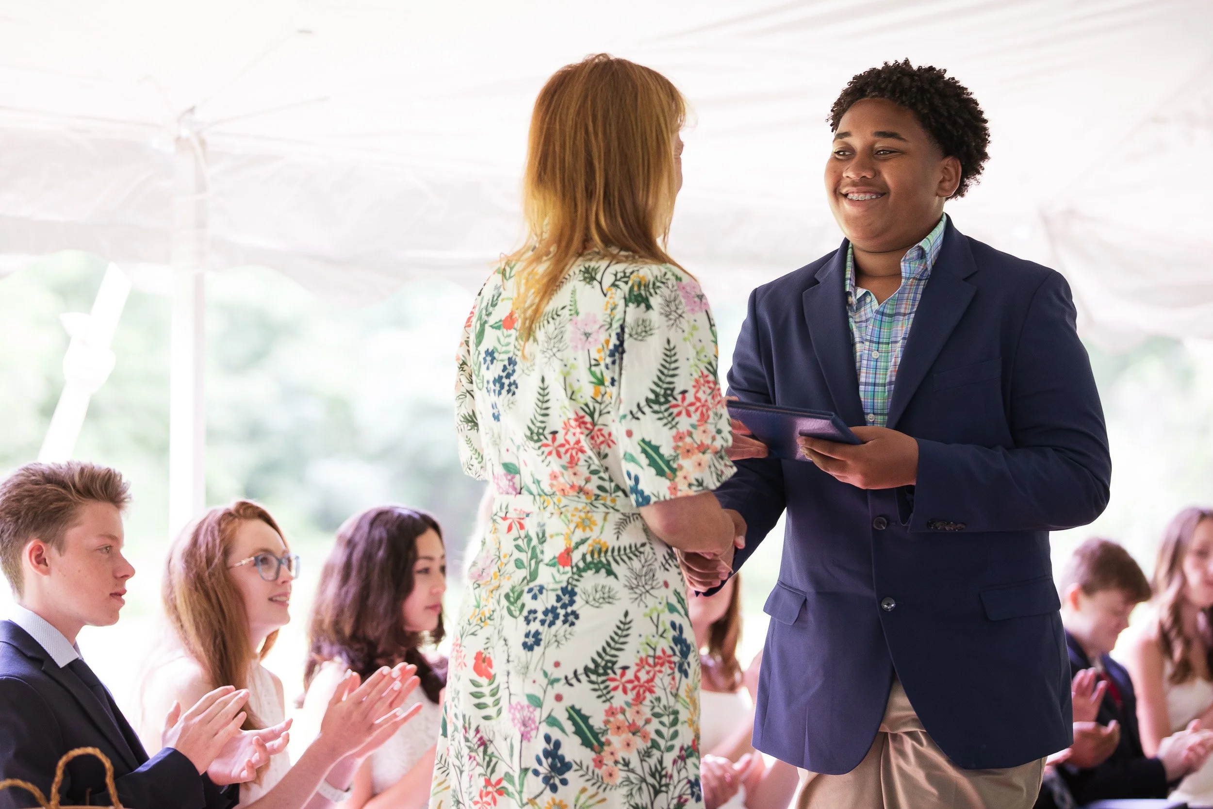 A young man in a blue blazer shaking hands with head of school during graduation ceremony.