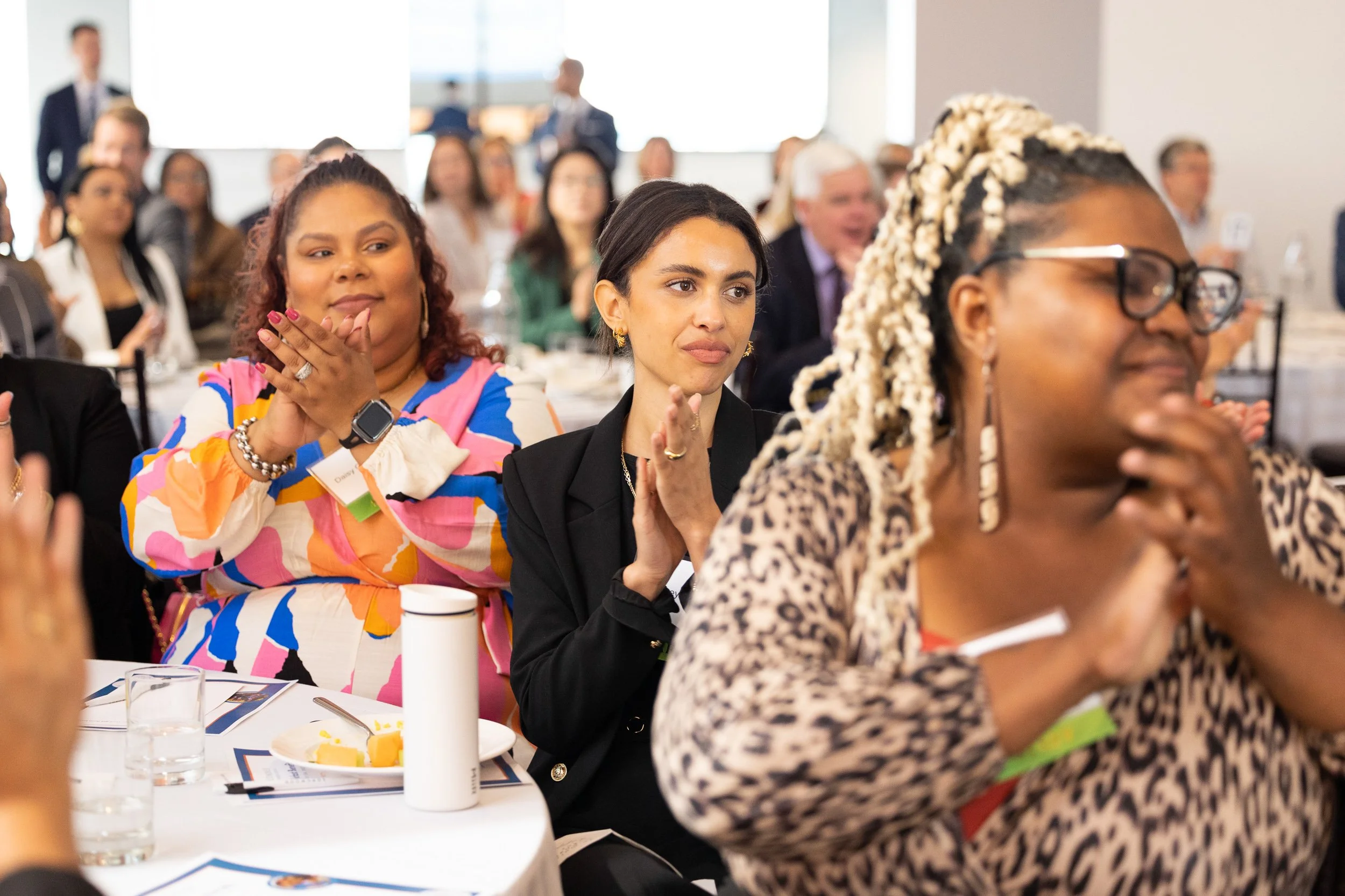 Attendees at a nonprofit event, sitting at round tables, clapping.
