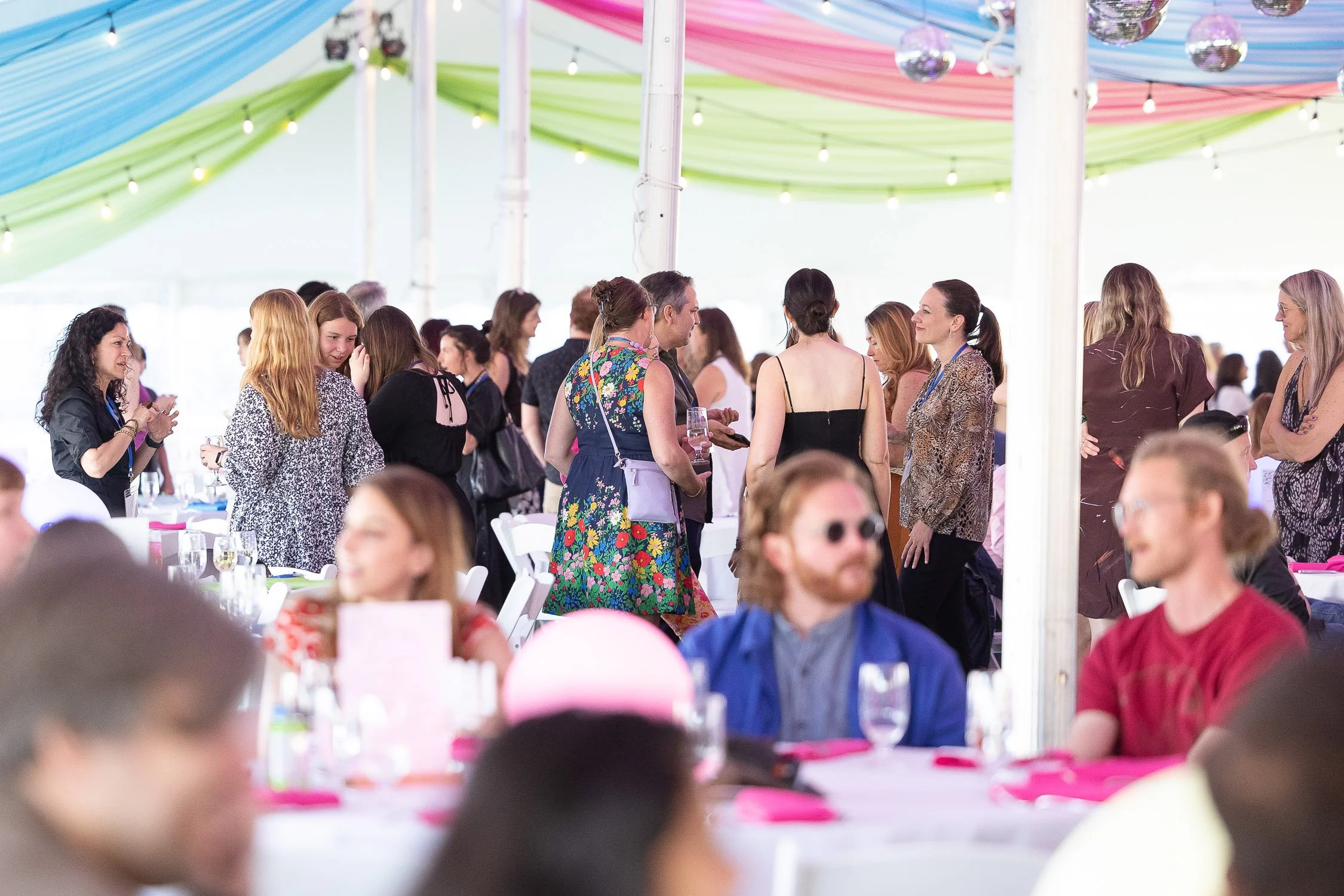 People socializing and standing under colorful draped decorations and string lights in a bright tent at the RISD reunion