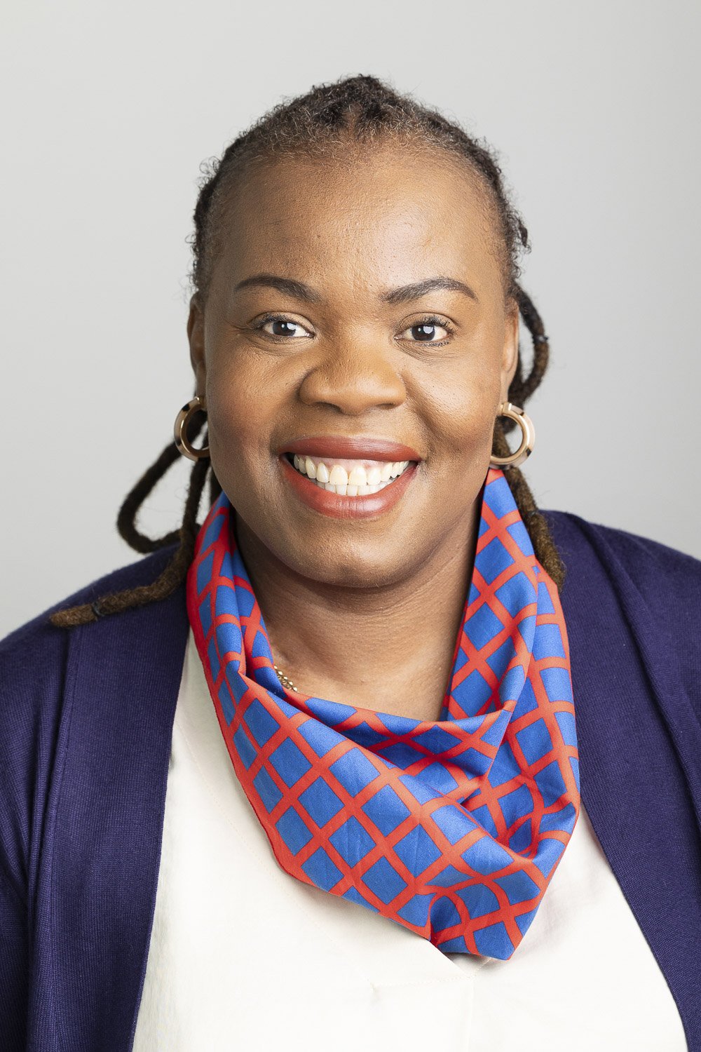 Portrait of a smiling woman wearing hoop a blue blazer and a colorful red and blue patterned scarf at a nonprofit organization in Boston, Massachusetts.