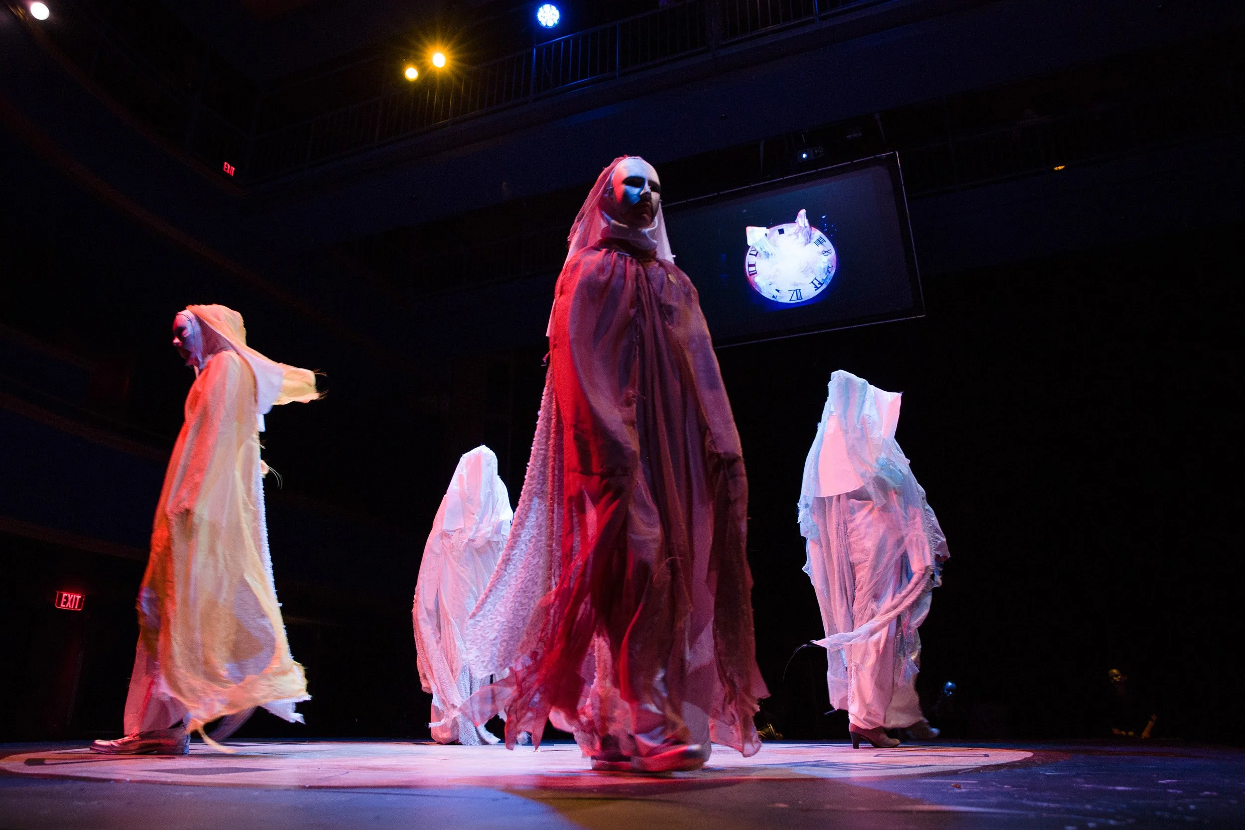A theatrical performance with four performers dressed in elaborate costumes with masks and flowing garments, at an independent high school in Massachusetts.