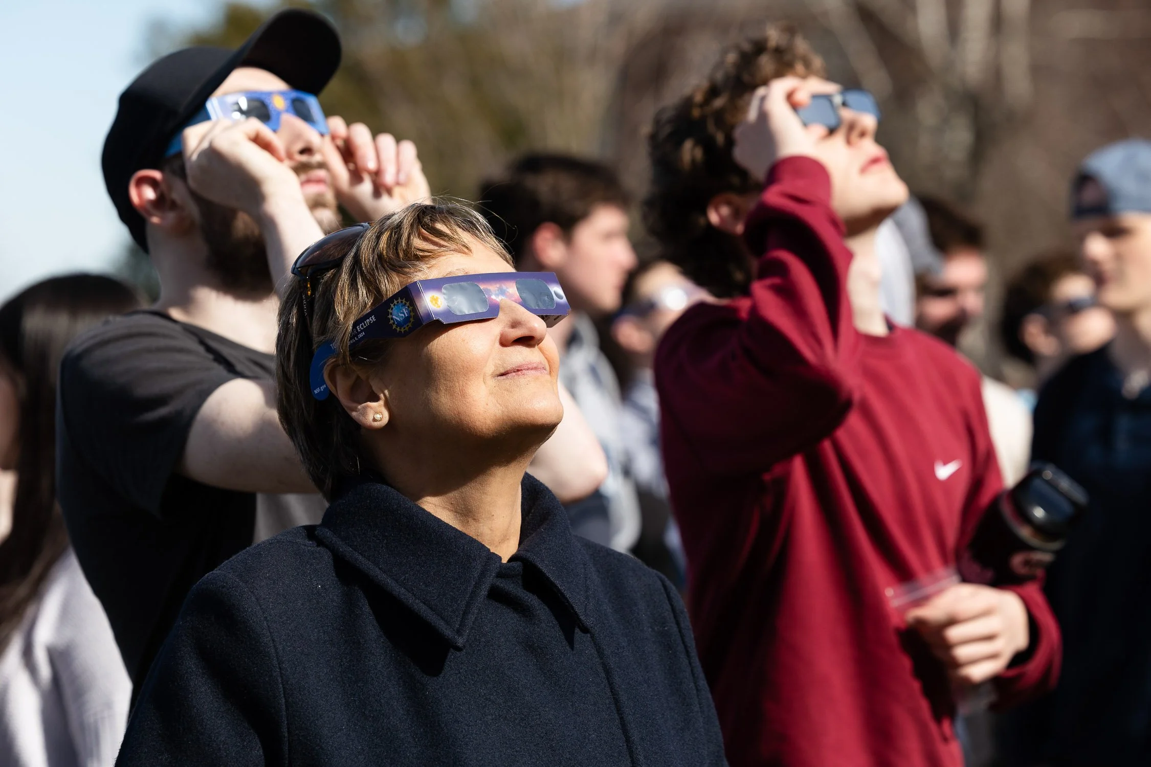 A group of people wearing eclipse glasses watching a solar eclipse at Saint Anselm College.